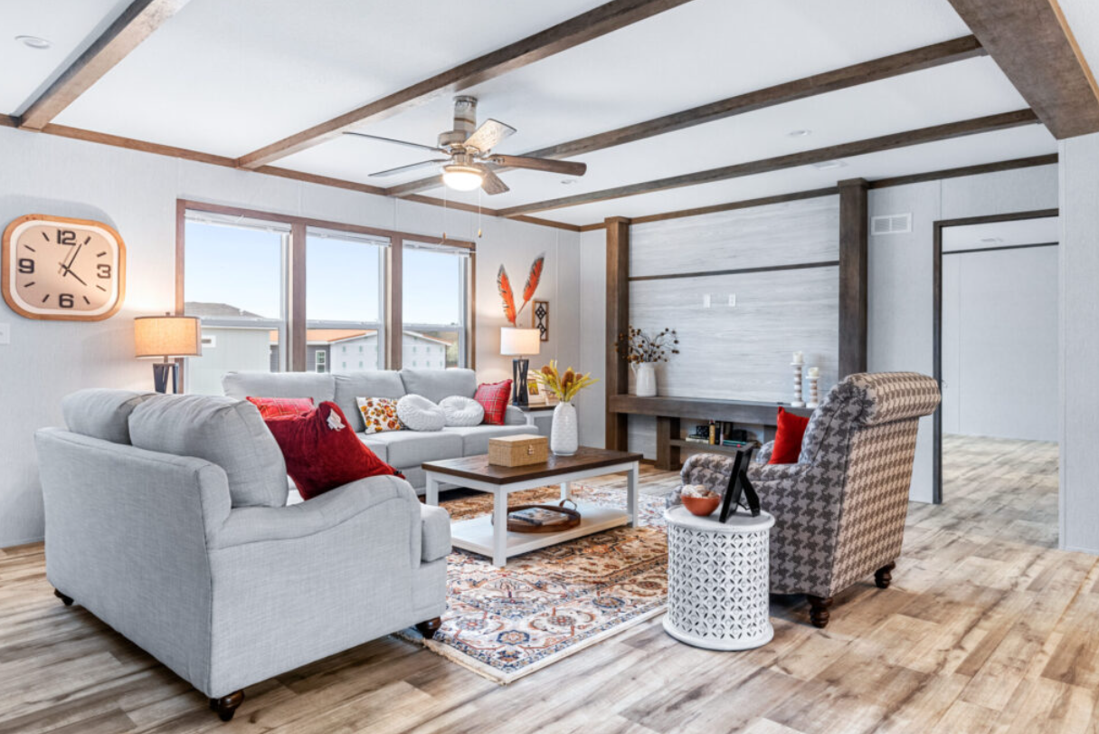 A bright living room with three sofas, colorful pillows, a coffee table, a rug, and large windows allowing natural light.