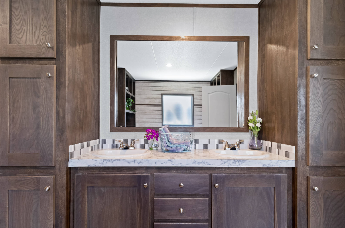 Bathroom vanity with a large mirror, dual sinks, and wooden cabinets, decorated with flowers and a towel basket.