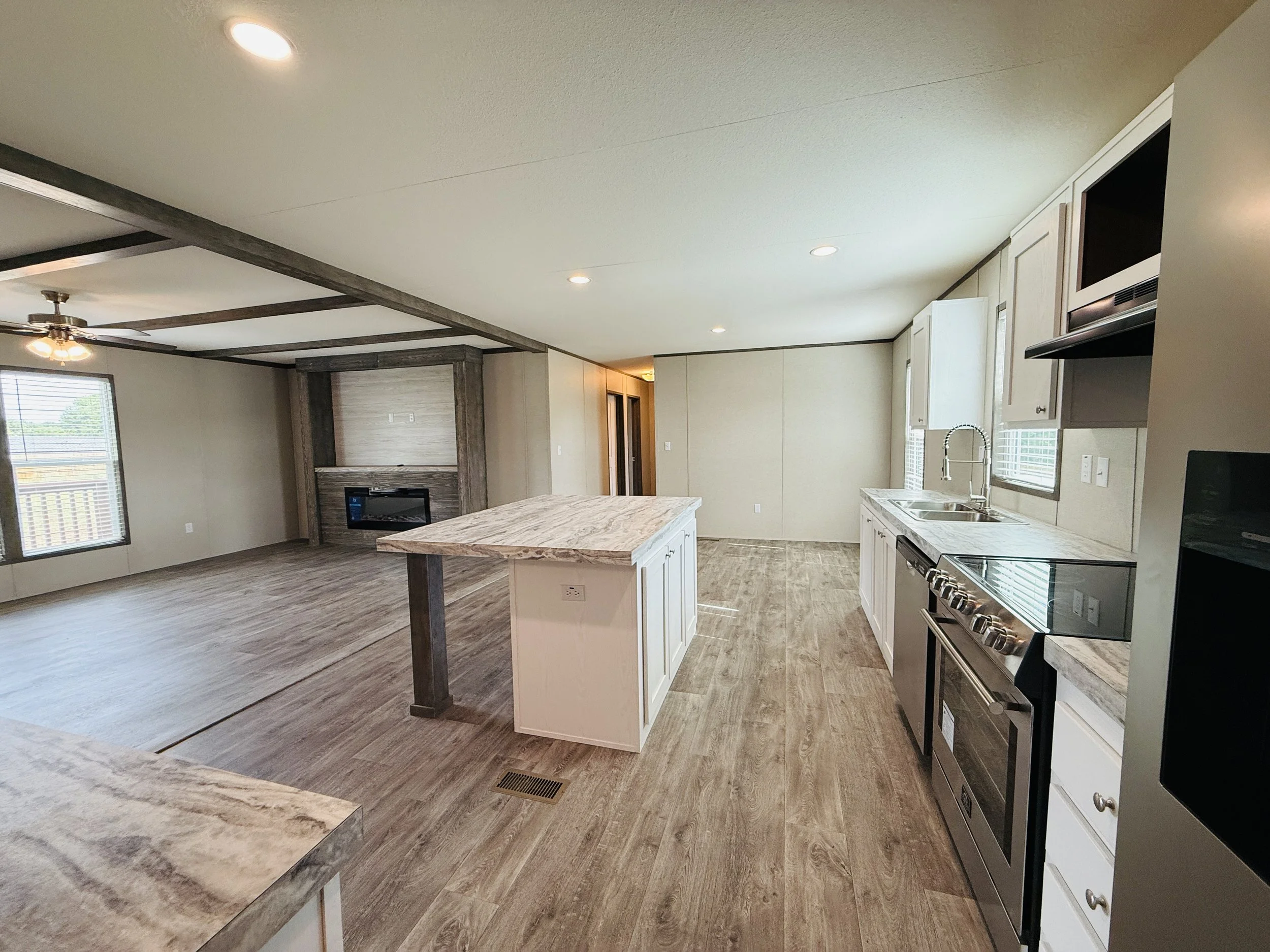 Open-concept kitchen and living room with wood flooring, white cabinets, stainless steel appliances, and a fireplace