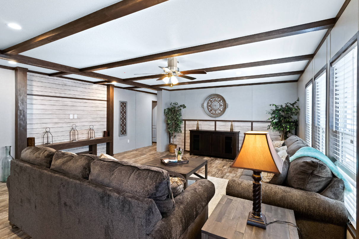 Living room with brown sofas, a coffee table, a lamp, a ceiling fan, plants, and large windows.