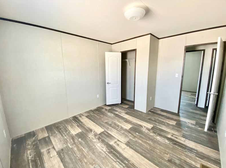 Empty room with wood-look flooring, closed closet door, and open doorway leading to another room.