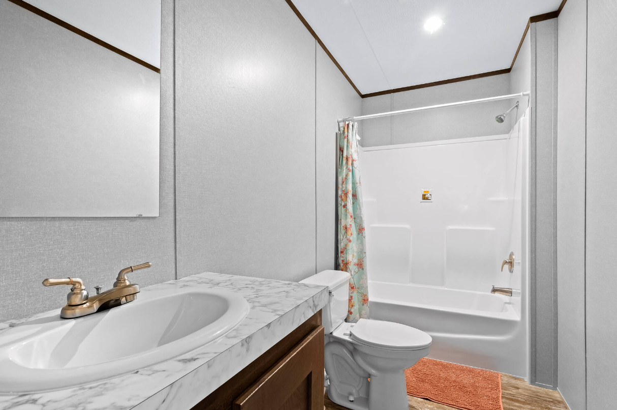 Bathroom with a marble countertop sink, gold faucet, toilet, bathtub with shower, and a floral shower curtain.