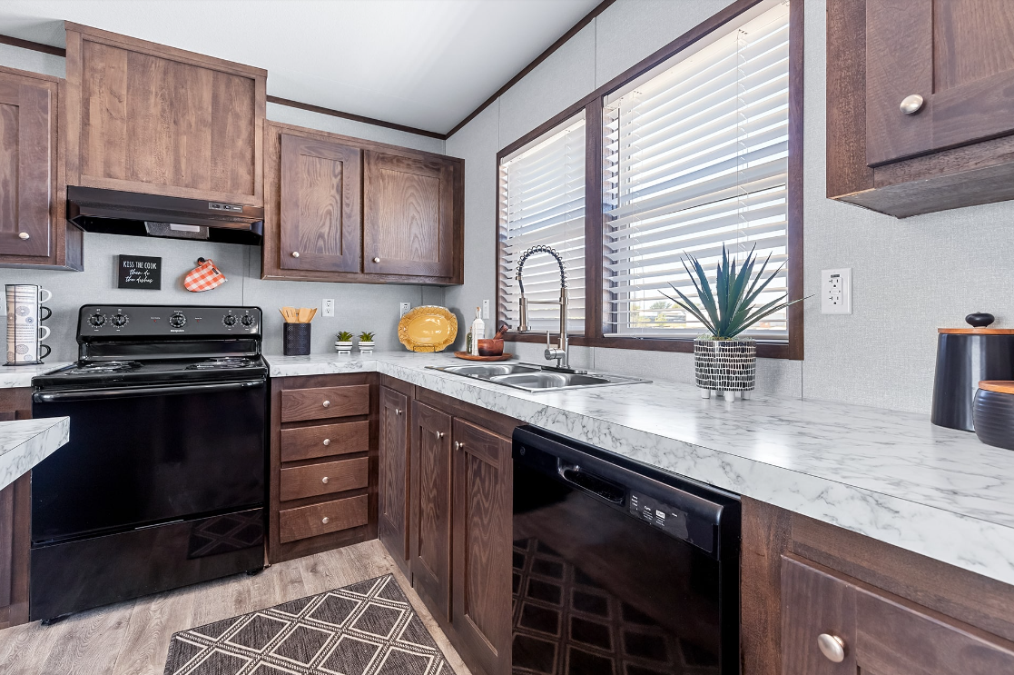 Kitchen with wooden cabinets, white marble countertops, black stove, dishwasher, and a window with blinds, decorated with potted plants and kitchen accessories.