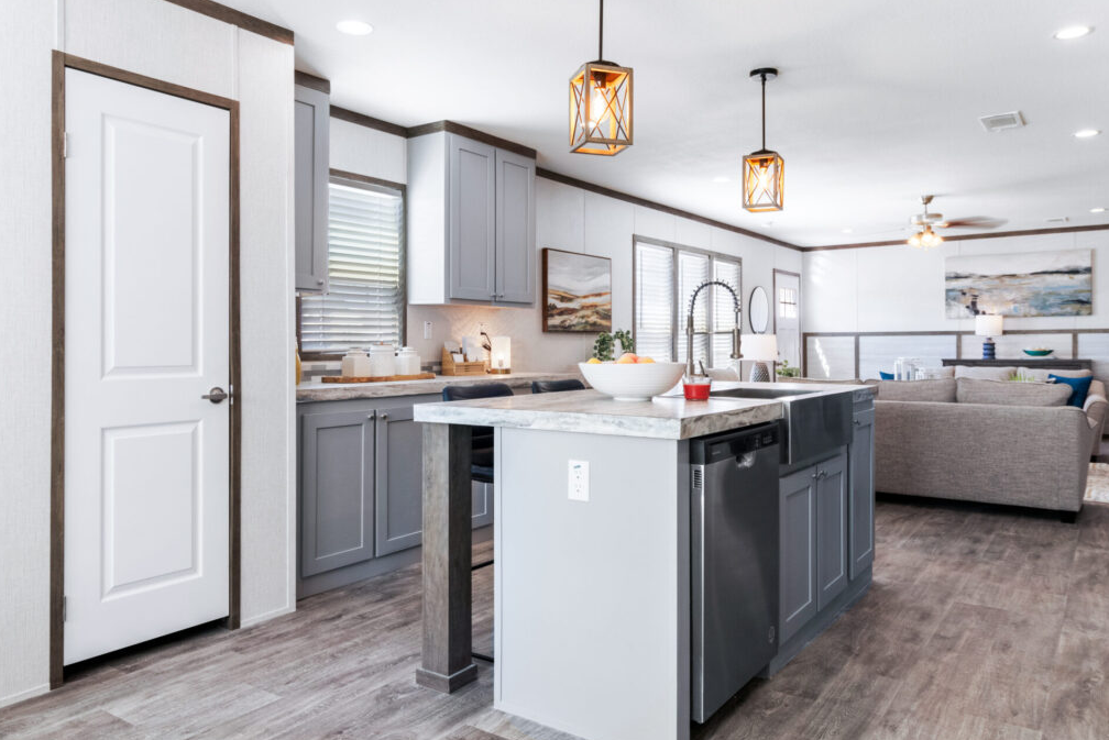 Modern kitchen with light gray cabinets, a white marble island, and pendant lighting, open to a living room with gray sofas and artwork.