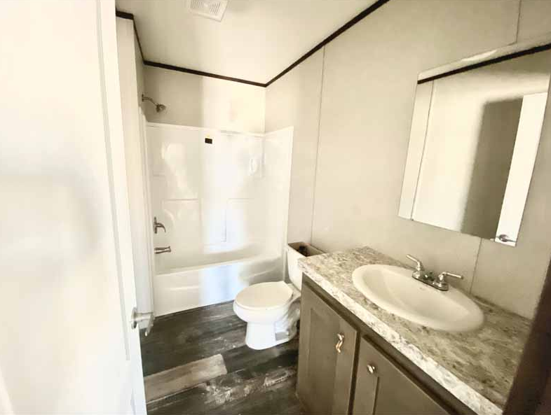 A bathroom with a bathtub and shower, a toilet, and a vanity with a marble countertop and a sink, with a mirror above it.
