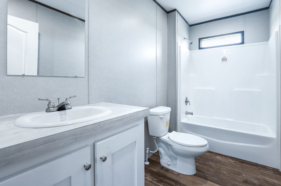 Bathroom with a white vanity sink, a mirror, a toilet, and a bathtub with a showerhead and a small window above.
