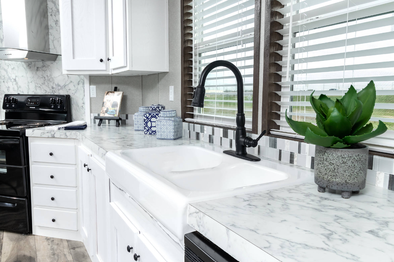 Kitchen sink area with a black faucet, white double basin sink, marble countertop, potted green succulent plant, blue decorative containers, and a window with blinds.