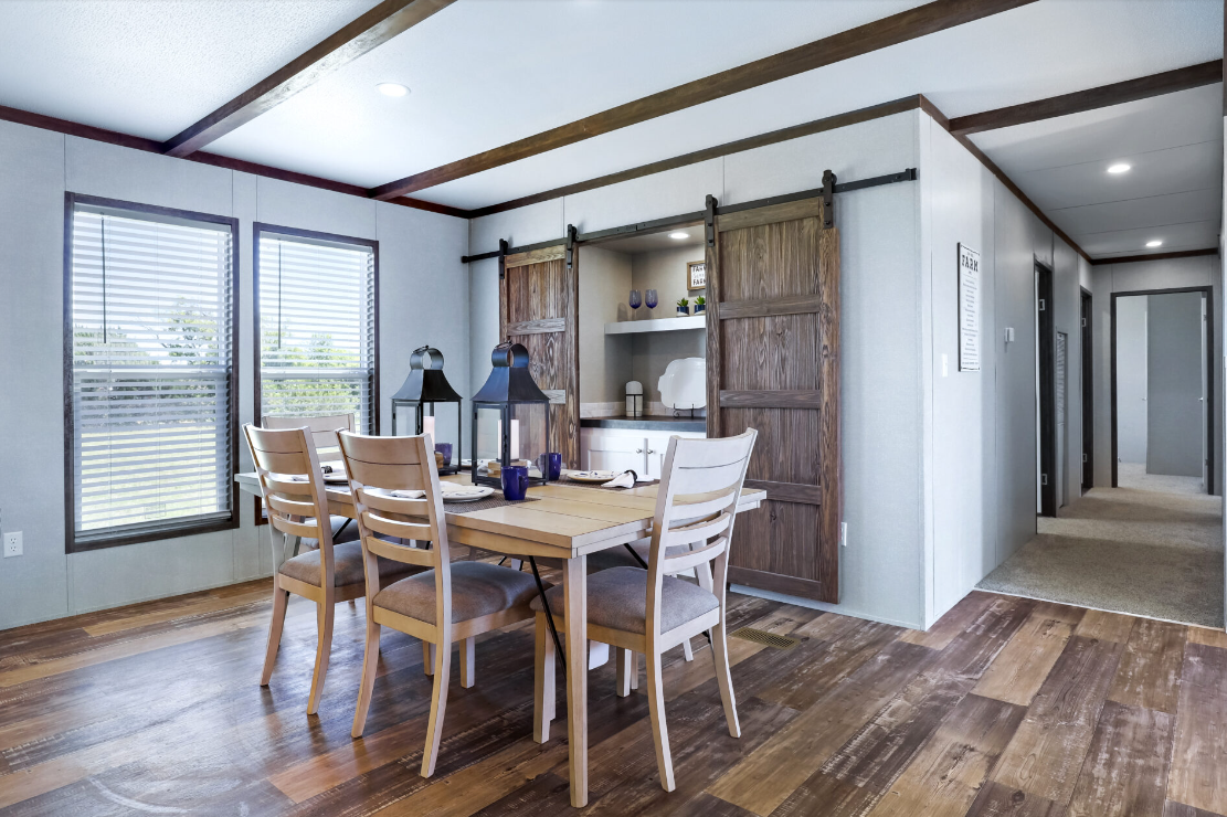 Dining room with wooden table, six chairs, two black lanterns, large windows, and a wooden sliding door leading to a kitchen or pantry area.