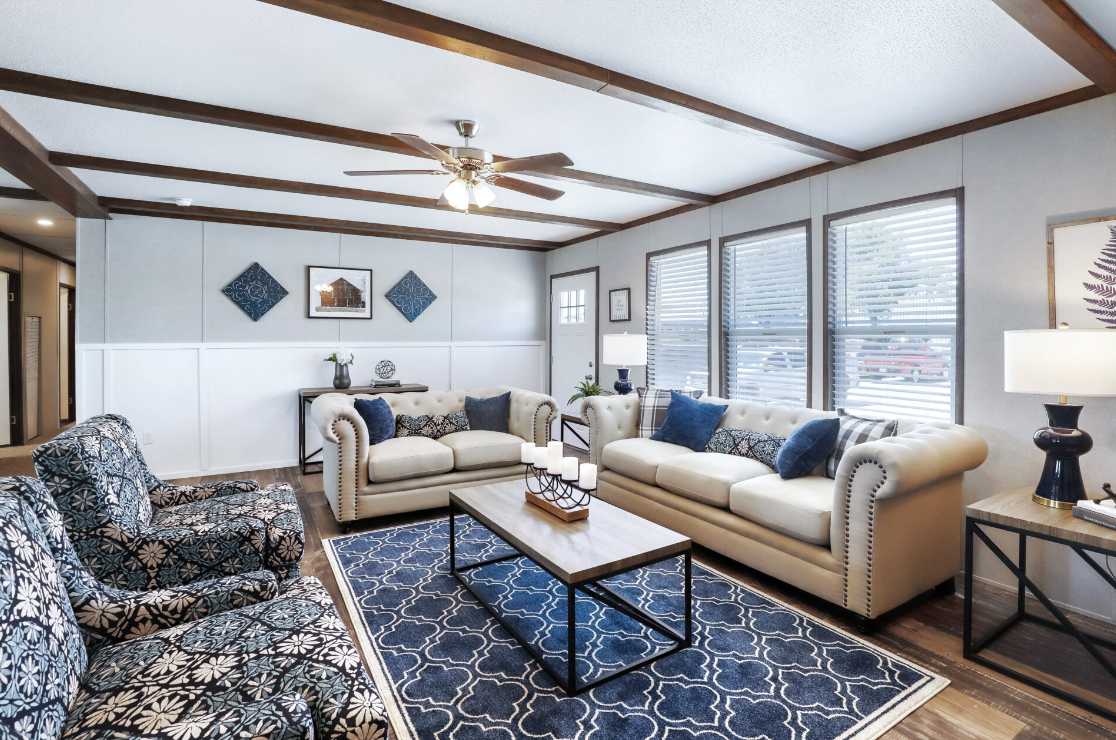 Living room with two white sofas, patterned armchairs, a rectangular coffee table, and large windows with blinds, decorated with blue and white accents.