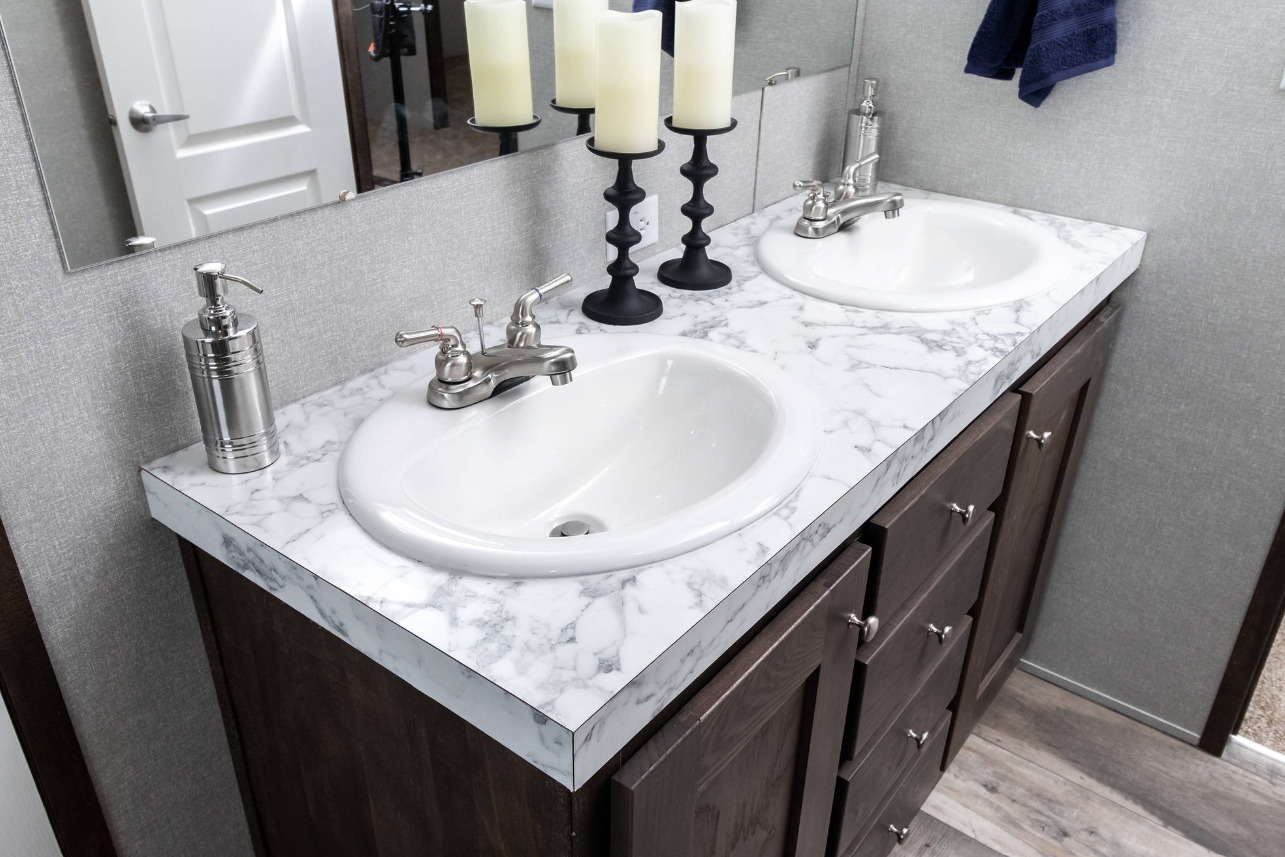 Double bathroom vanity with marble countertop, two sinks, silver faucets, a soap dispenser, three candles on black candlesticks, and a mirror above the sinks.