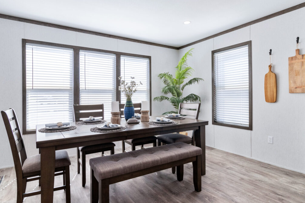 Dining room with a wooden table, chairs, a bench, window blinds, a plant, and wall decor.