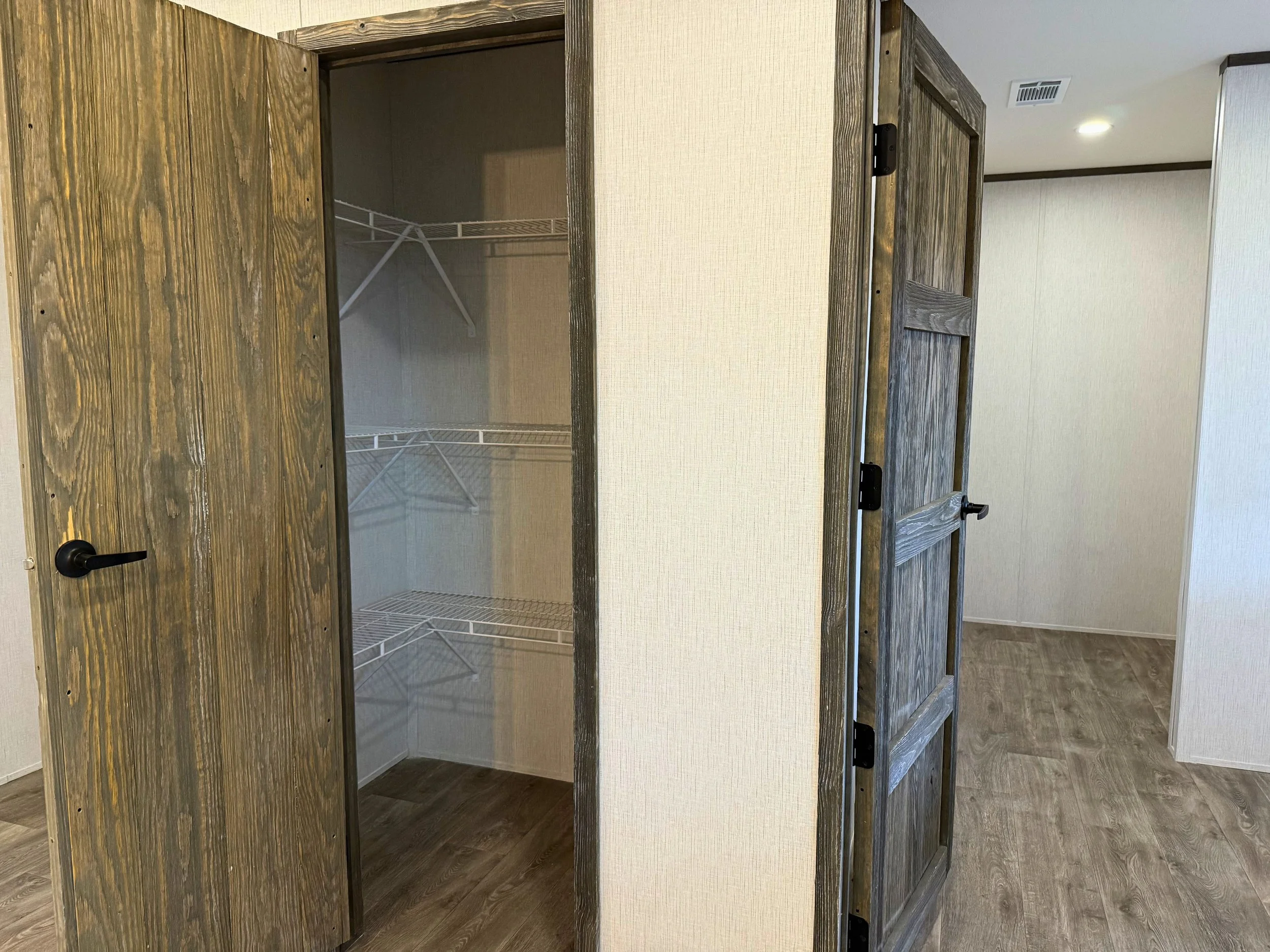 Empty closet with open door, wire shelves inside, in a room with wood flooring and textured light-colored walls.