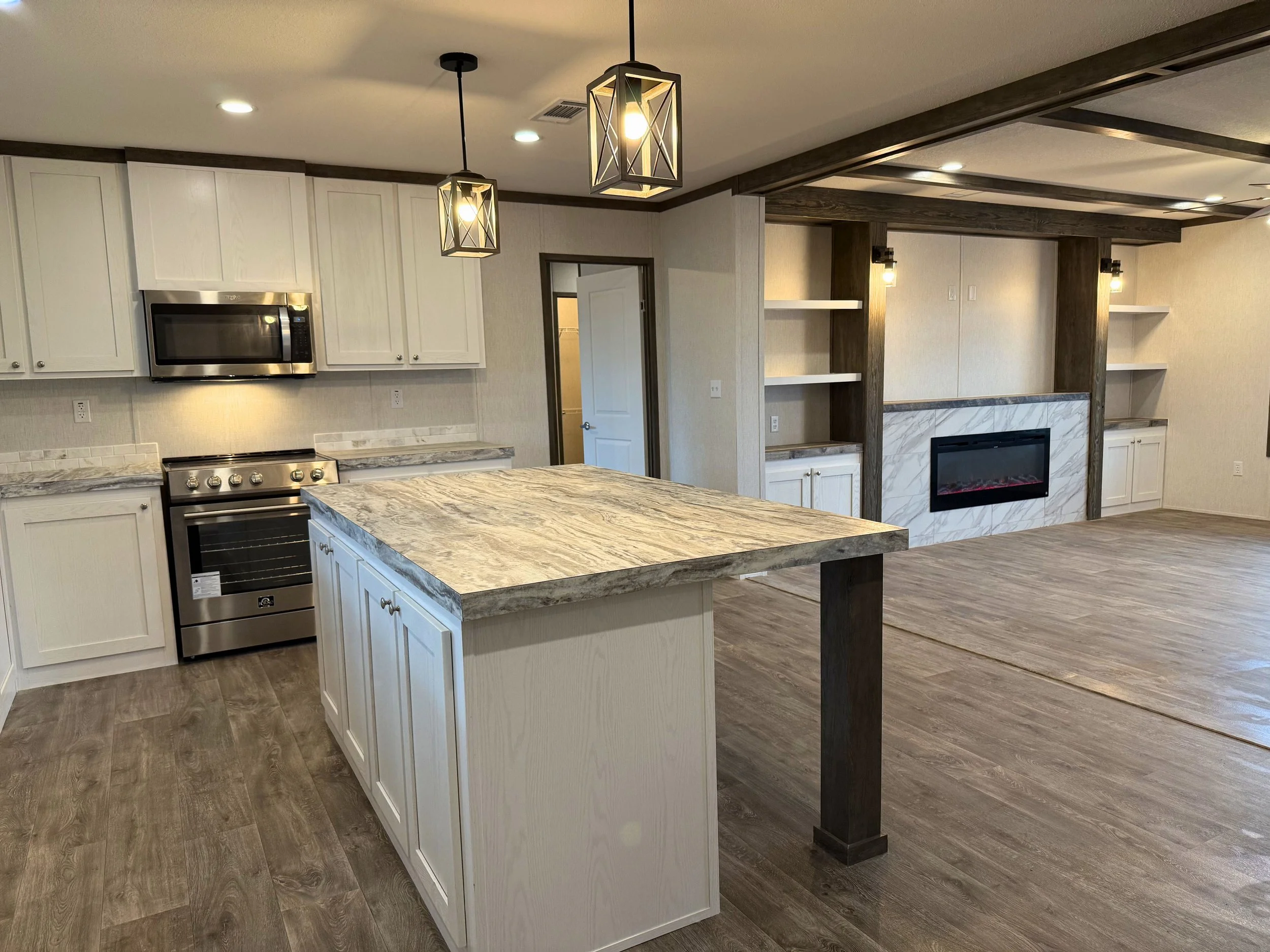 Open-concept kitchen and living room with white cabinets, stainless steel appliances, a marble kitchen island, and a fireplace with a marble surround, wood accents, and built-in shelves.