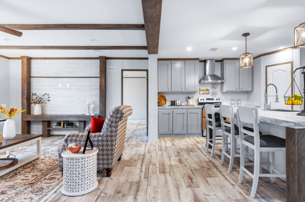 Open-concept living room and kitchen with light gray cabinets, white walls, wood accents, and hardwood floors.