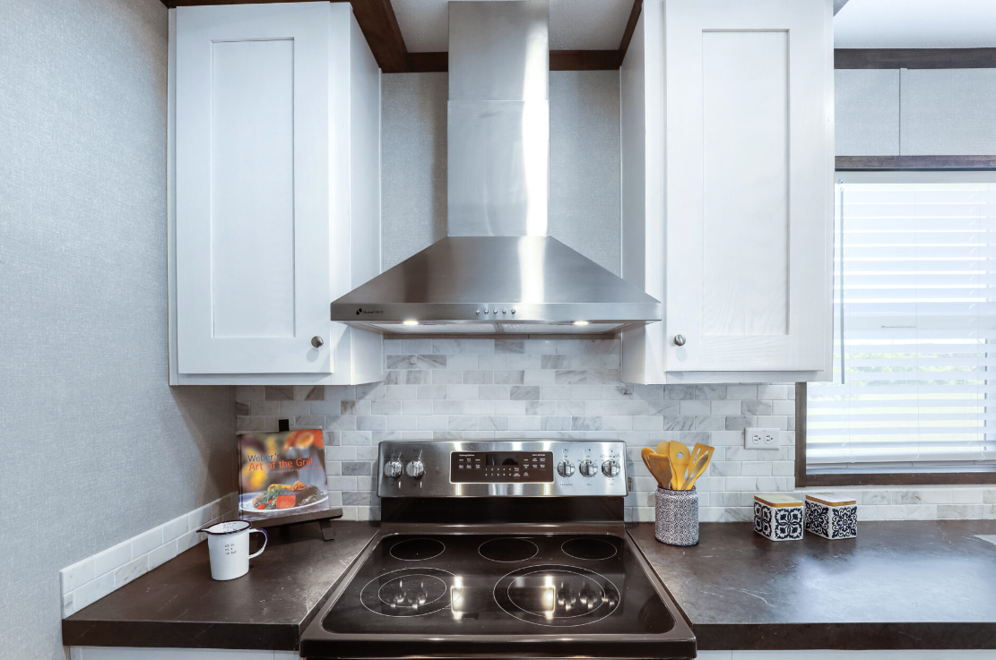 Modern kitchen with white cabinets, stainless steel range hood, and black electric stove, with a window on the right side.