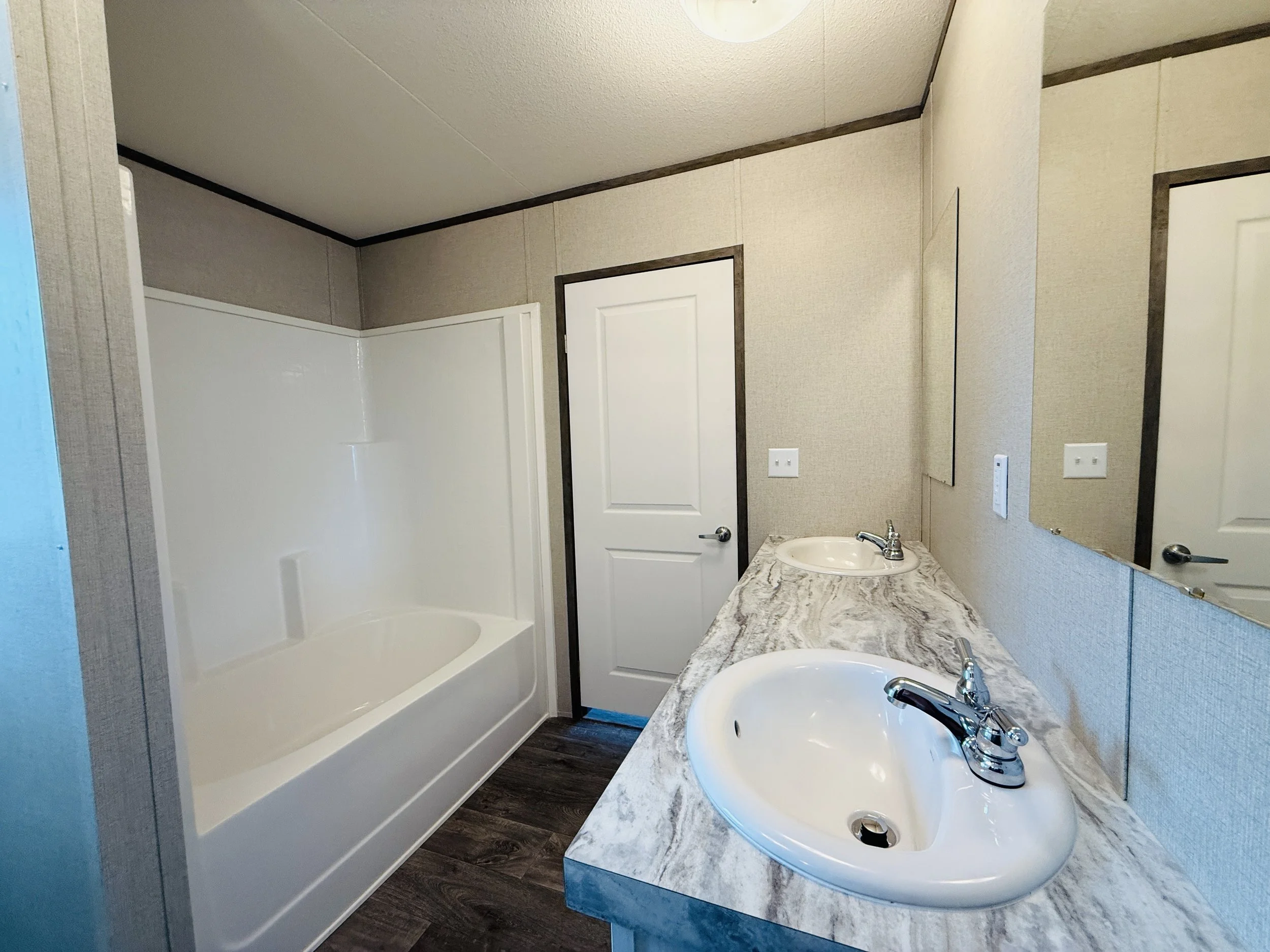 Bathroom with a bathtub, a marble countertop with two sinks, and mirrors. The walls are beige with dark trim, and there are two white doors.