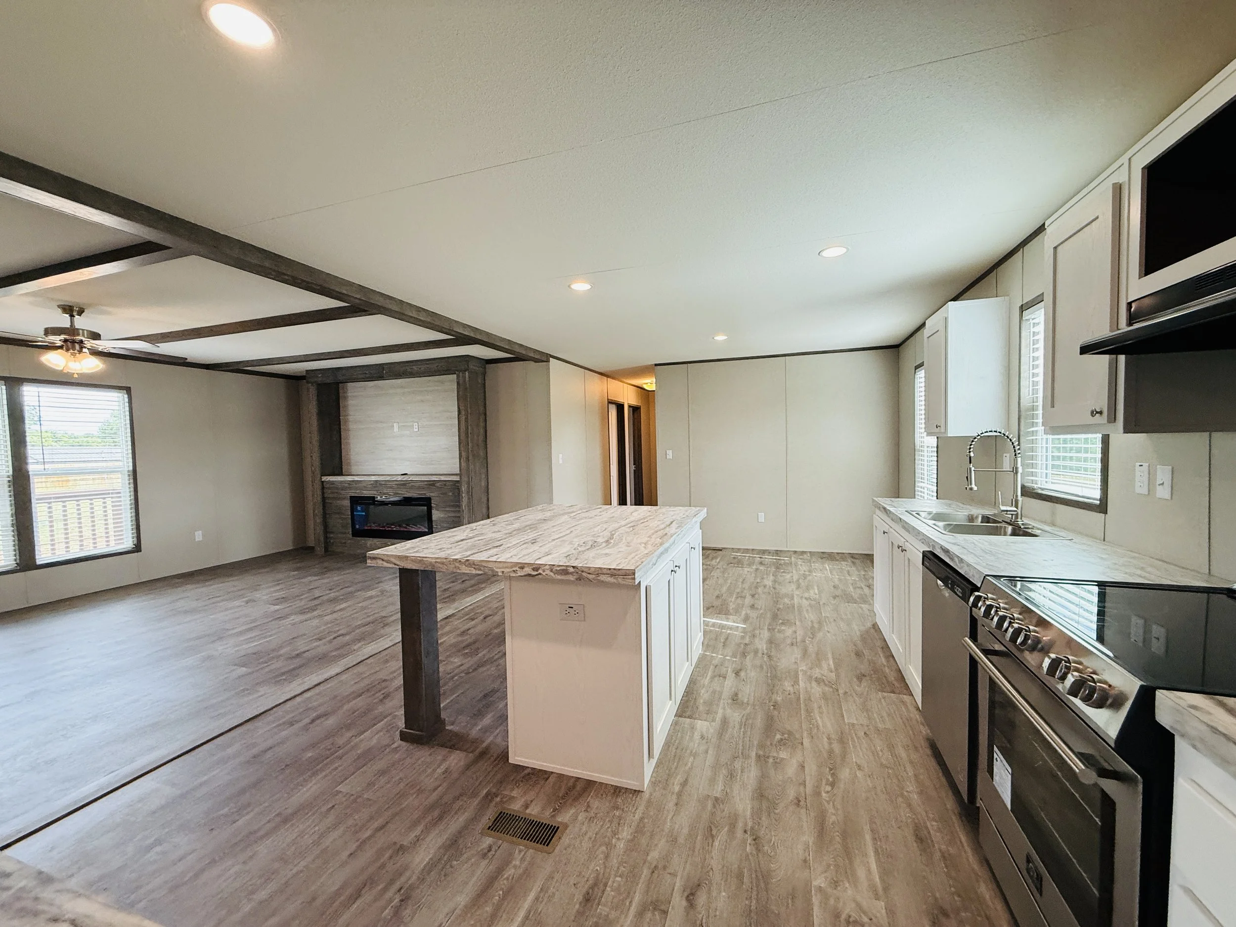 Open-concept living space with kitchen and living area, featuring white cabinets, a marble island, stainless steel stove, and a fireplace with a wooden mantel.