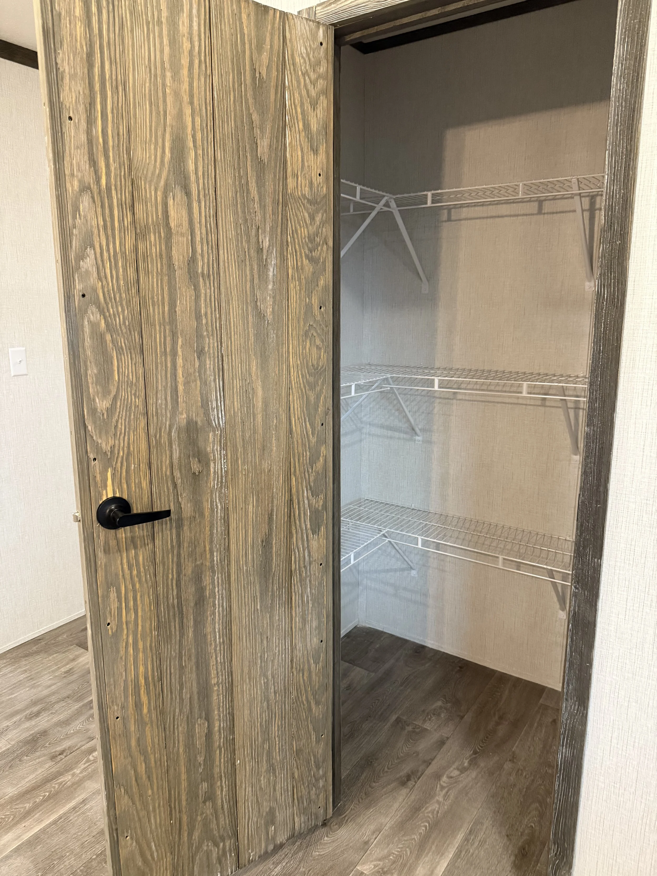 Empty closet with wire shelves and a partially open rustic wood door.