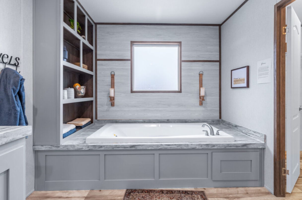 Bathroom with a bathtub, open shelves with towels and toiletries, a window above the tub, wall sconces with candles, and a framed picture on the wall.