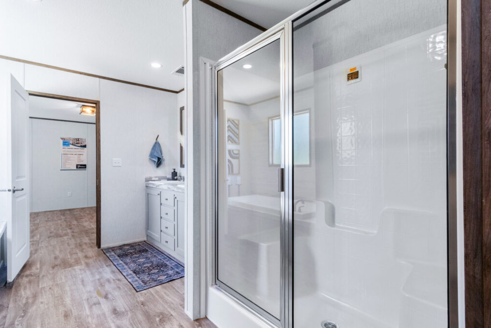 Bathroom with glass shower enclosure, white vanity with drawers, towel hanging on the wall, and a window providing natural light.