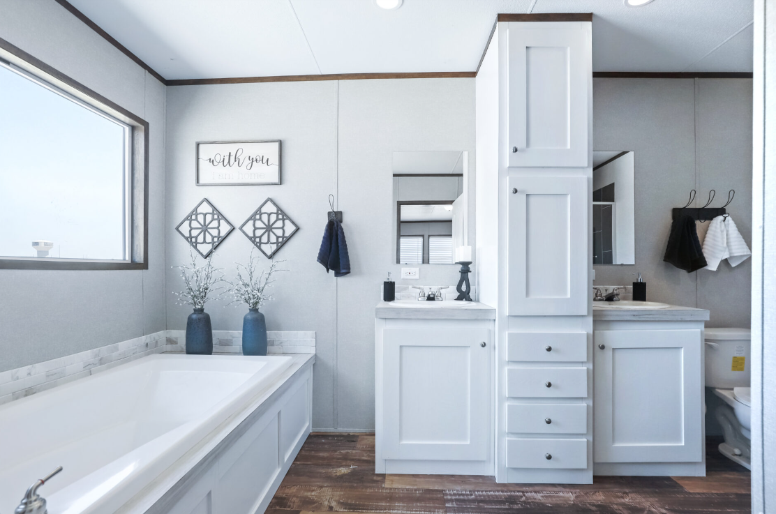 Bathroom with white cabinets, a bathtub, a sink with a mirror, towels on hooks, and decorative vases with branches.