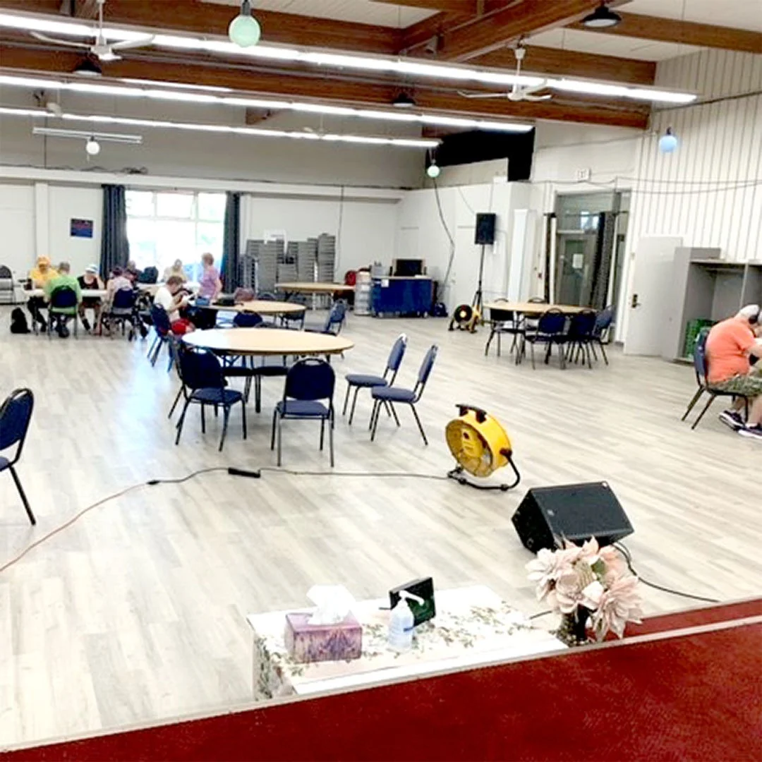 Wide image of a bright auditorium space with banquet tables and chairs set up and people sitting in the distance