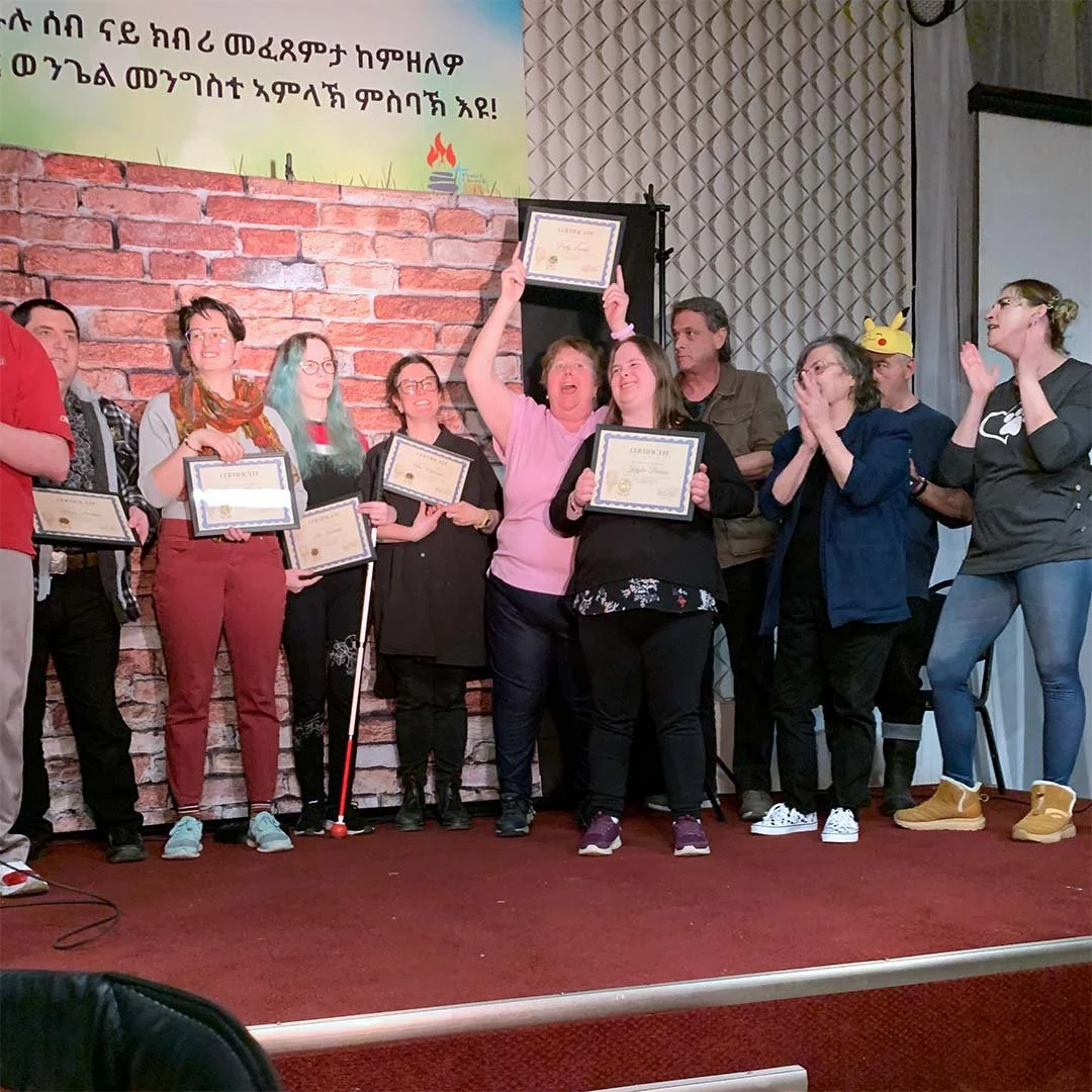 A group of community members hold certificates and cheer on stage