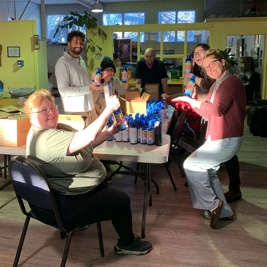 Community members pose and smile for the camera as they work together around a table