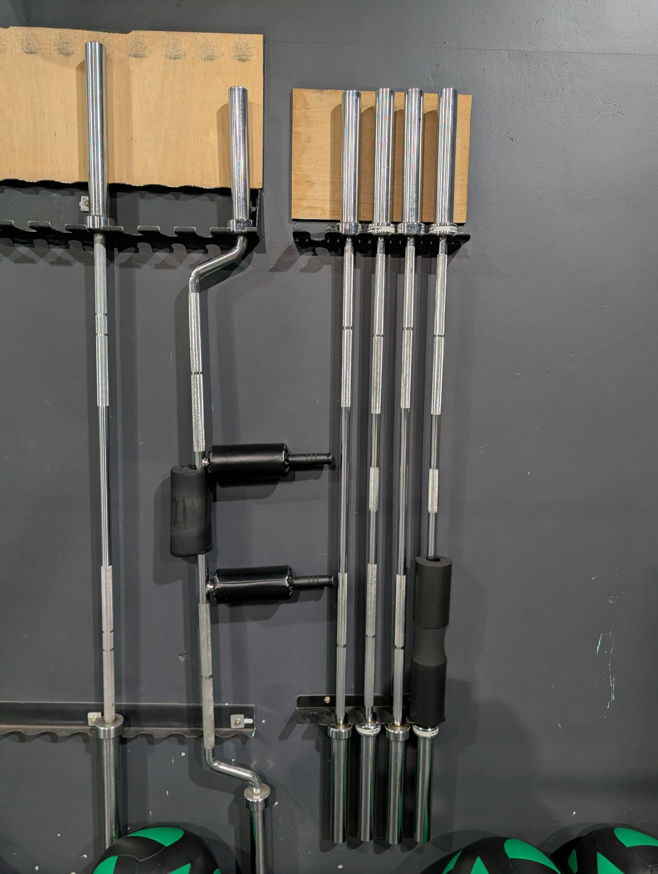 Set of six metal sledgehammers with black handles, mounted on a gray wall with wooden panels.