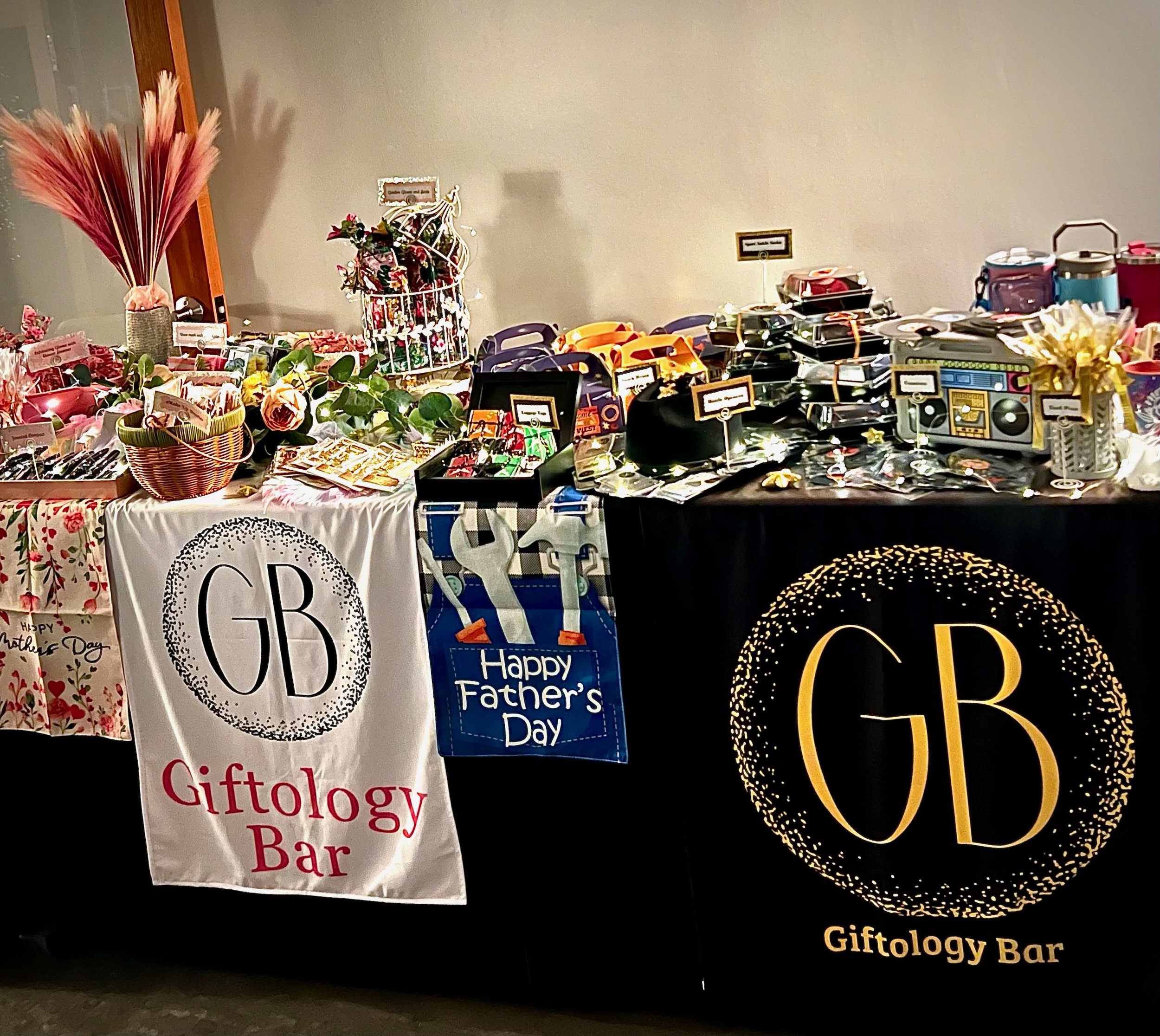 Display table for 'Giftology Bar' with various gift items for occasions like Father's Day, including baskets, decorations, and gift boxes.