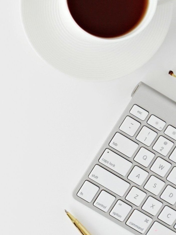 Top view of a coffee cup, computer keyboard, and pen on a white background.