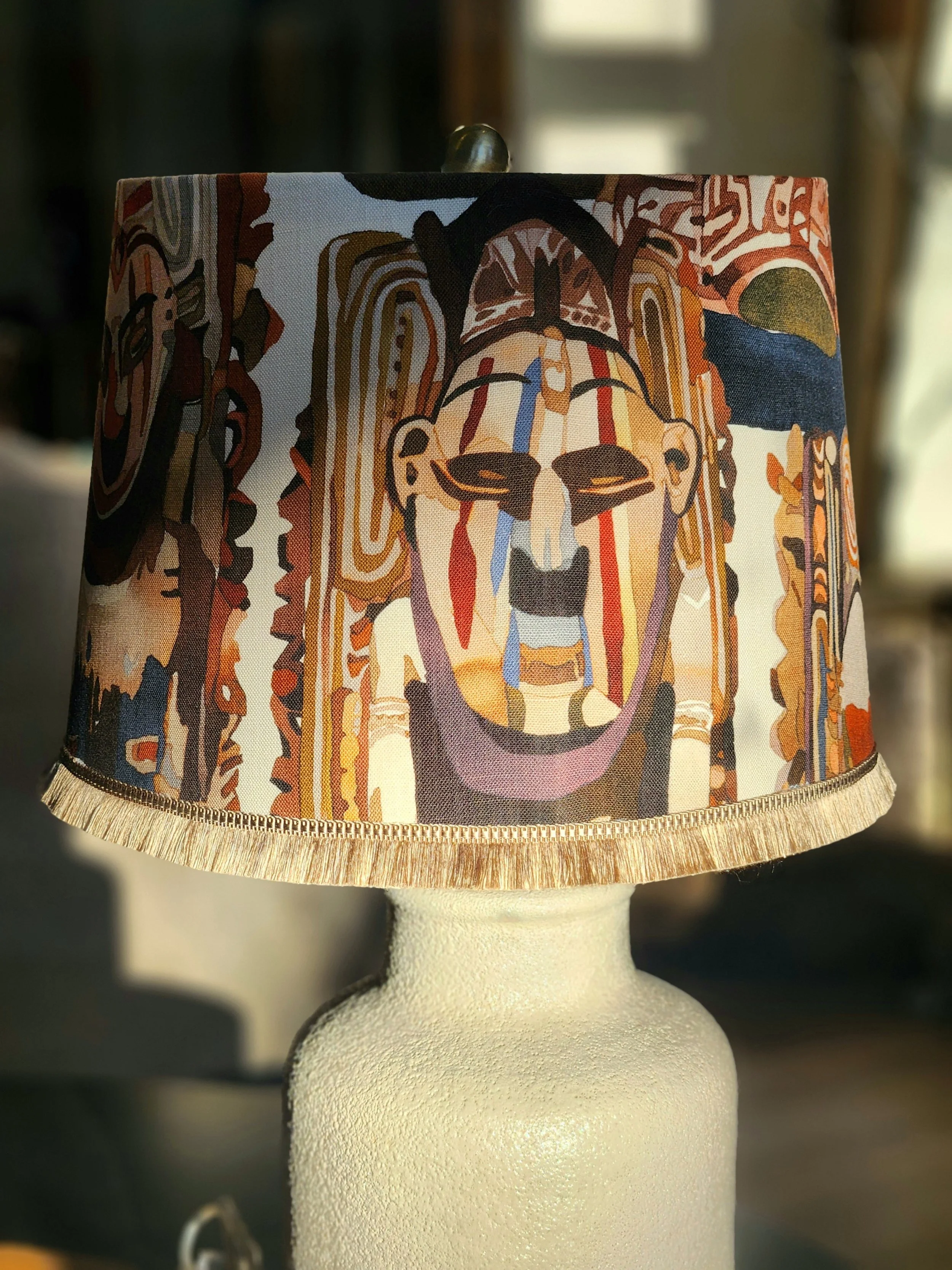 Table lamp with a colorful lampshade featuring a tribal mask design.