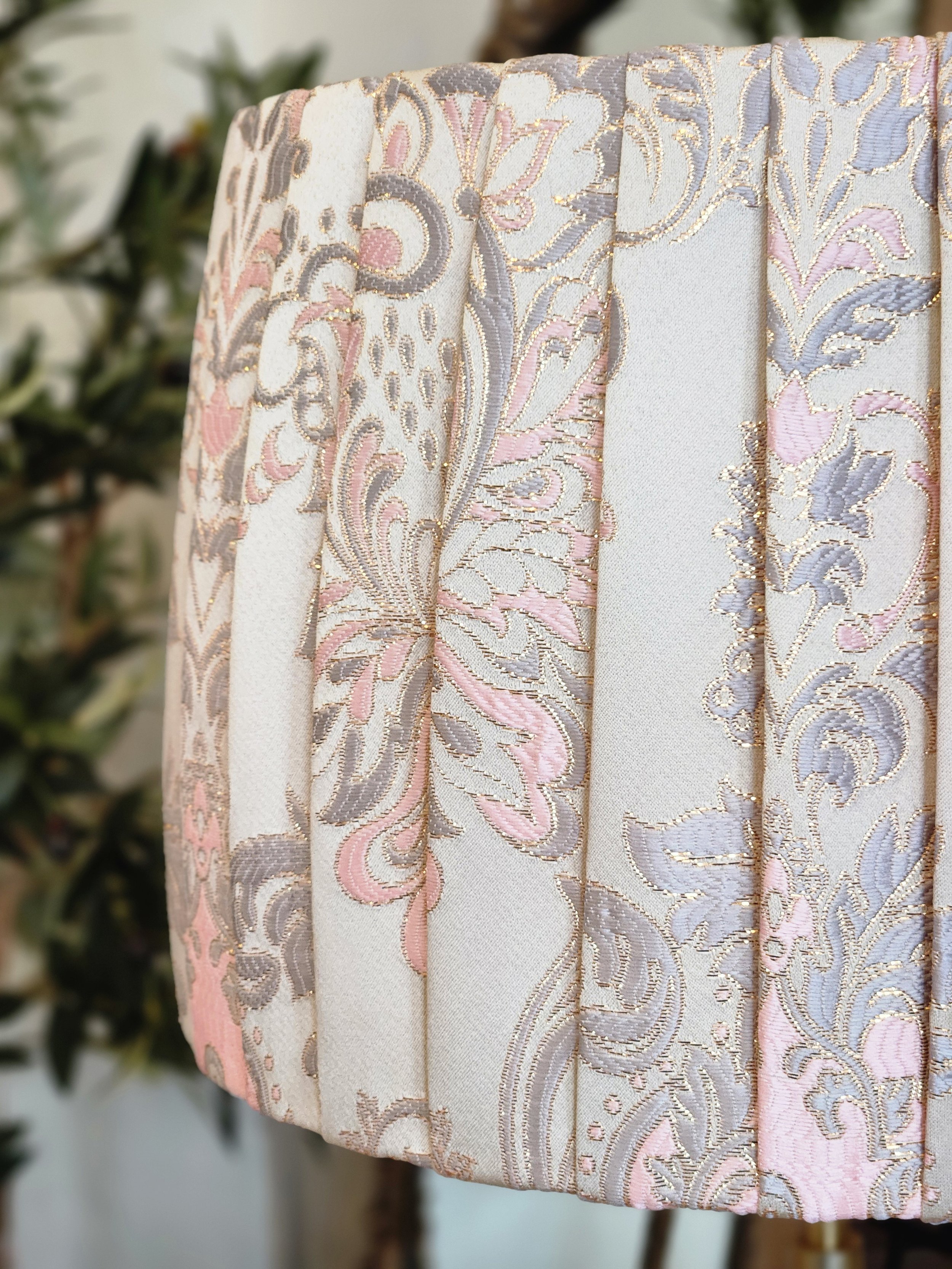 Close-up of a pleated lampshade with a cream fabric and a pink, blue, and gold floral damask pattern. The pleats add texture and dimension to the shade.