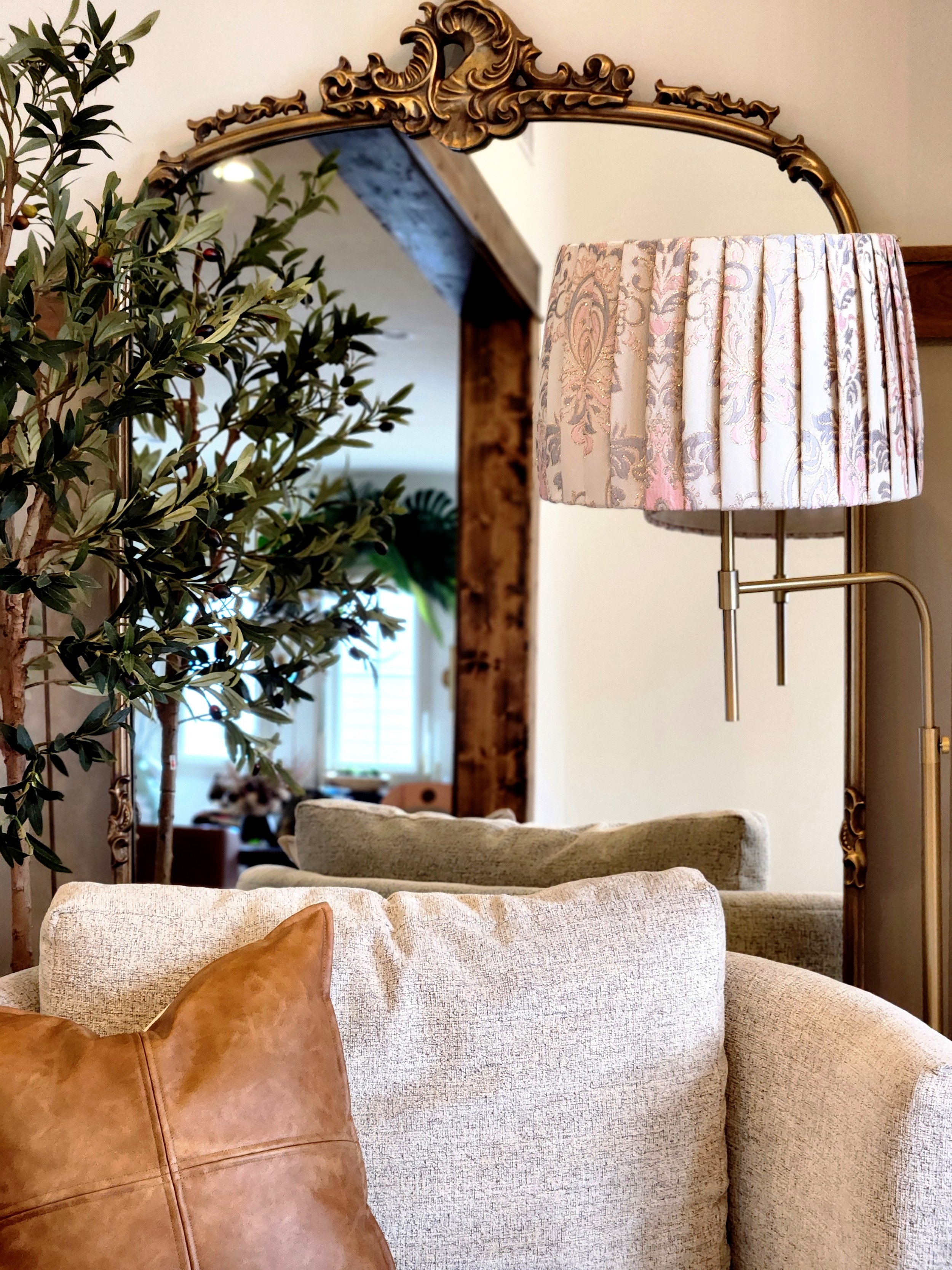 A pleated lampshade with a delicate floral pattern in pink and blue hues. It sits atop a floor lamp positioned in front of an ornate mirror.