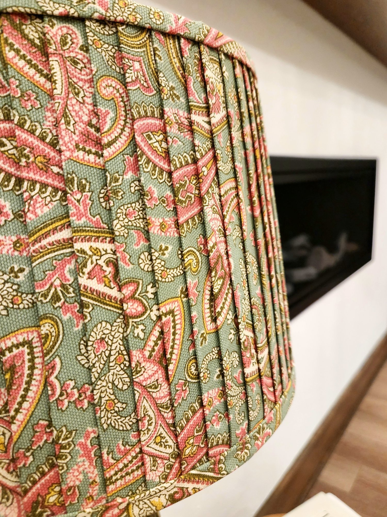 Close-up of a sage green lampshade with a pink and gold paisley pattern. The pleated fabric adds texture and visual interest to the shade.