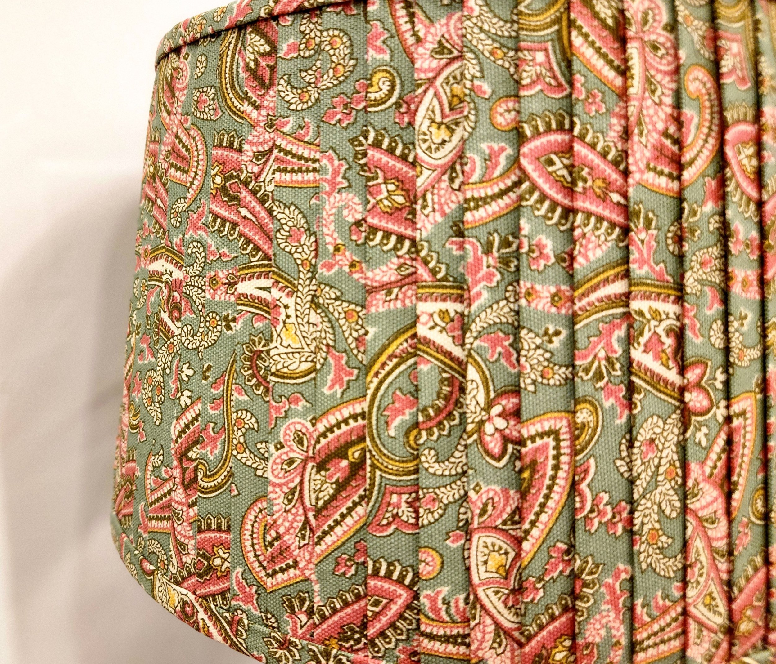 Close-up of a sage green lampshade with a pink and gold paisley pattern. The pleated fabric adds texture and visual interest to the shade.