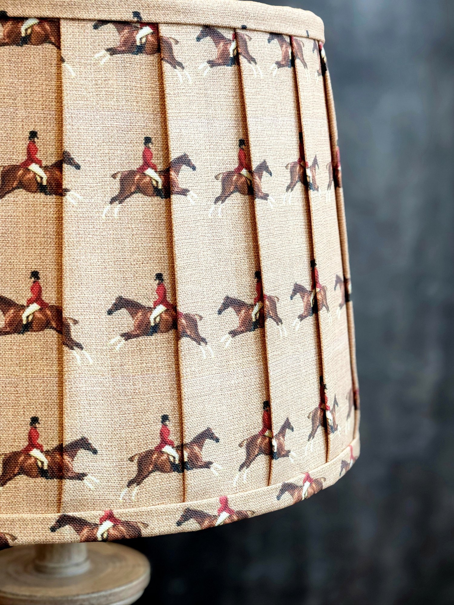 Close-up of a tan lampshade with a repeating pattern of a jockey on a horse. The fabric is pleated, creating vertical lines between each image.
