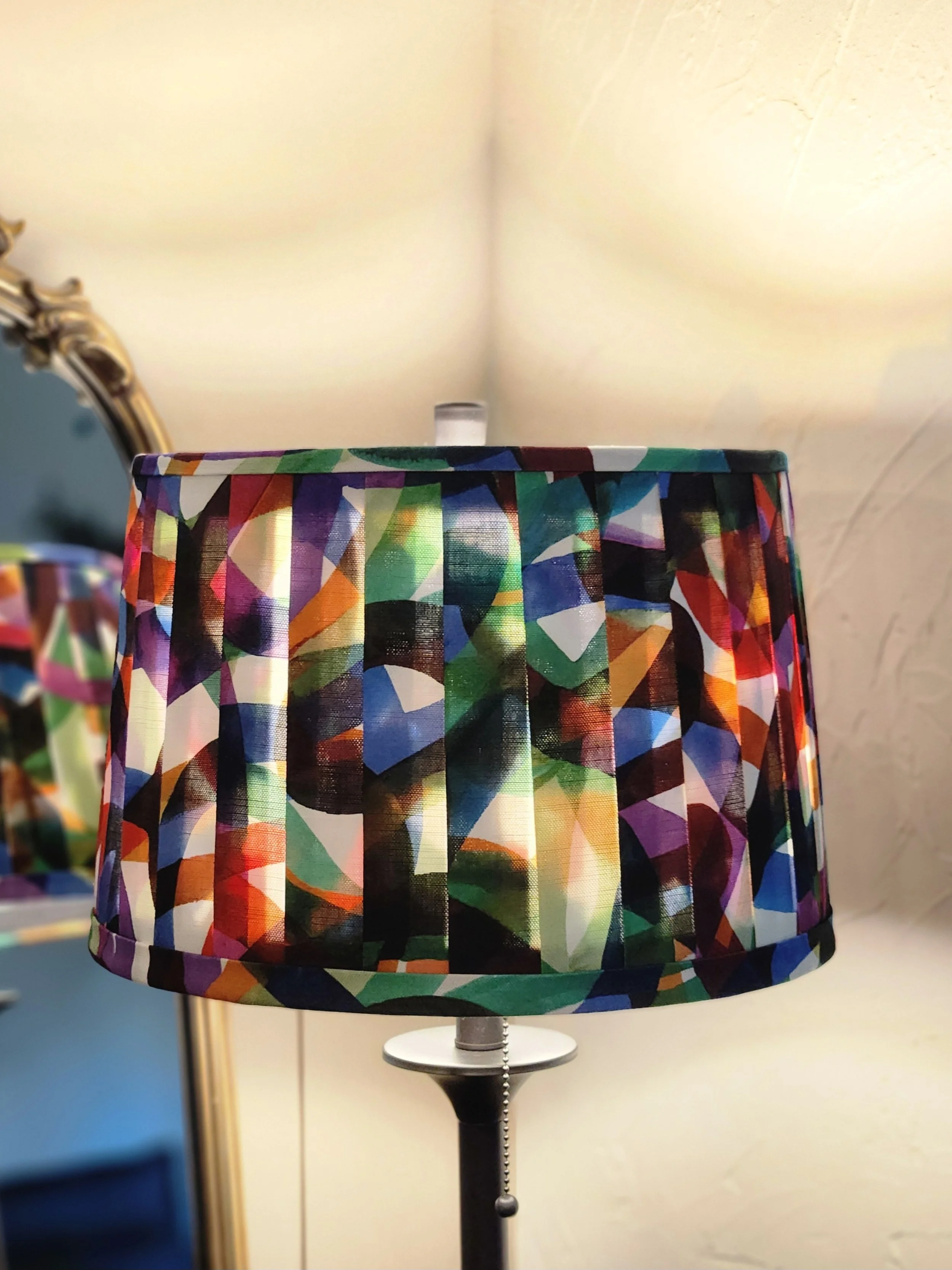 A lampshade with a bold, abstract pattern in a vibrant mix of colors. The pleated design adds depth and texture.