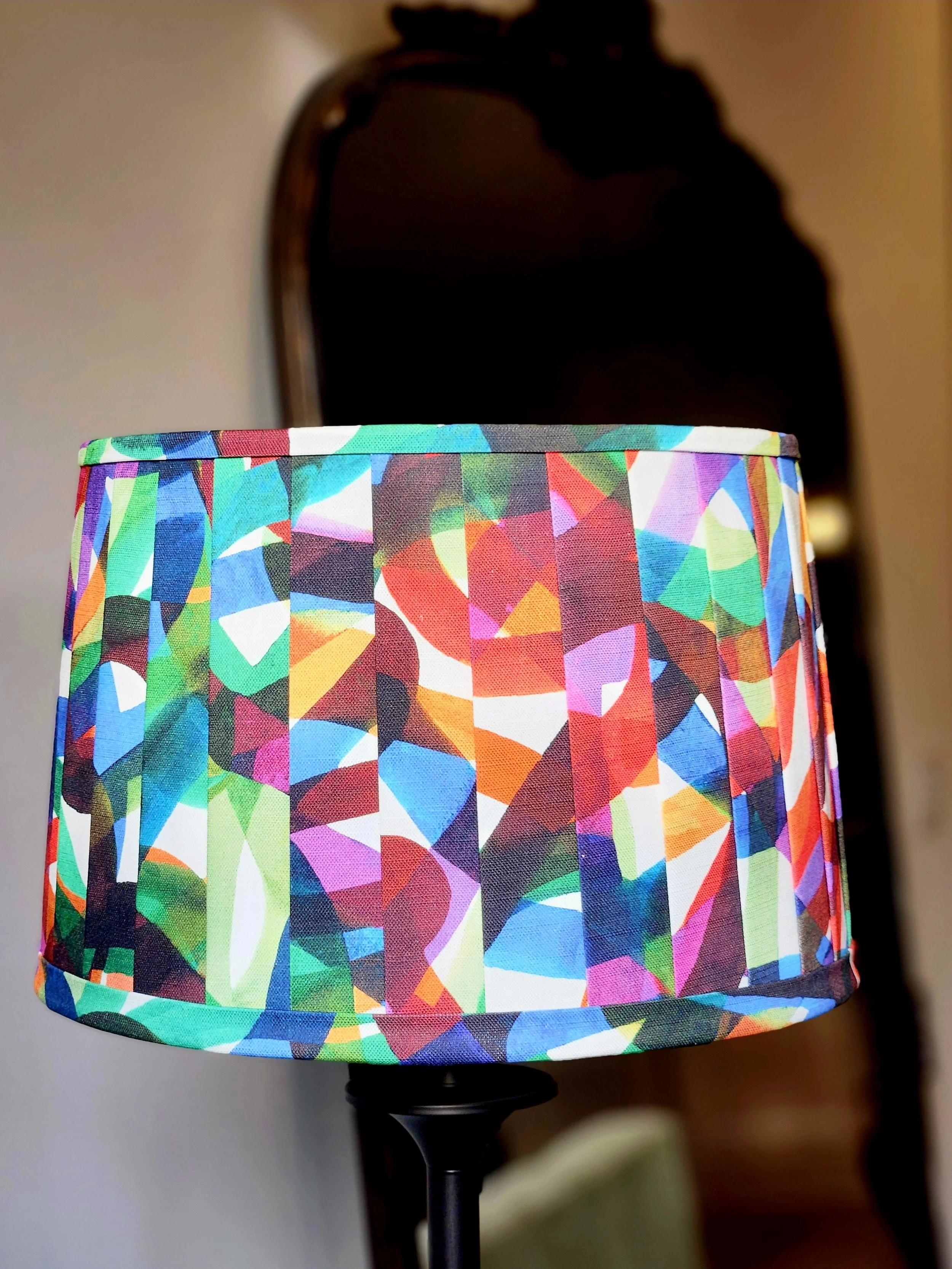A lampshade featuring a vibrant, abstract pattern in a kaleidoscope of colors. The pleated design adds a dynamic element to this statement piece.