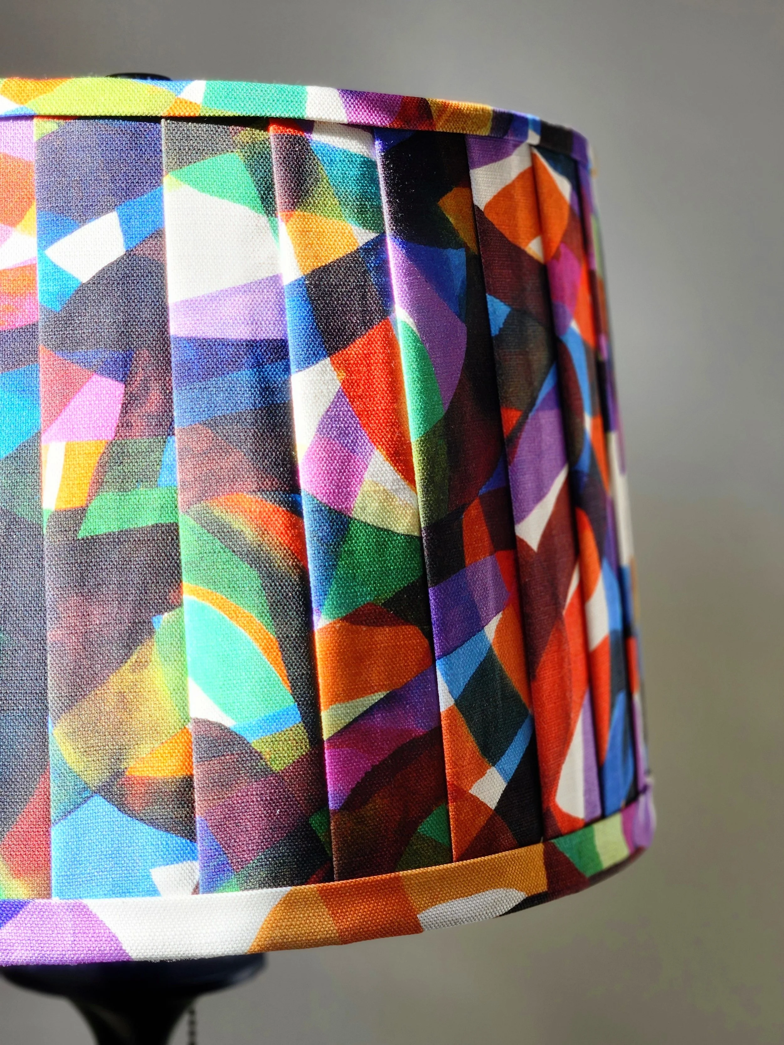 Close-up of a lampshade with a vibrant, abstract pattern in a kaleidoscope of colors. The texture and detail of the fabric are highlighted.