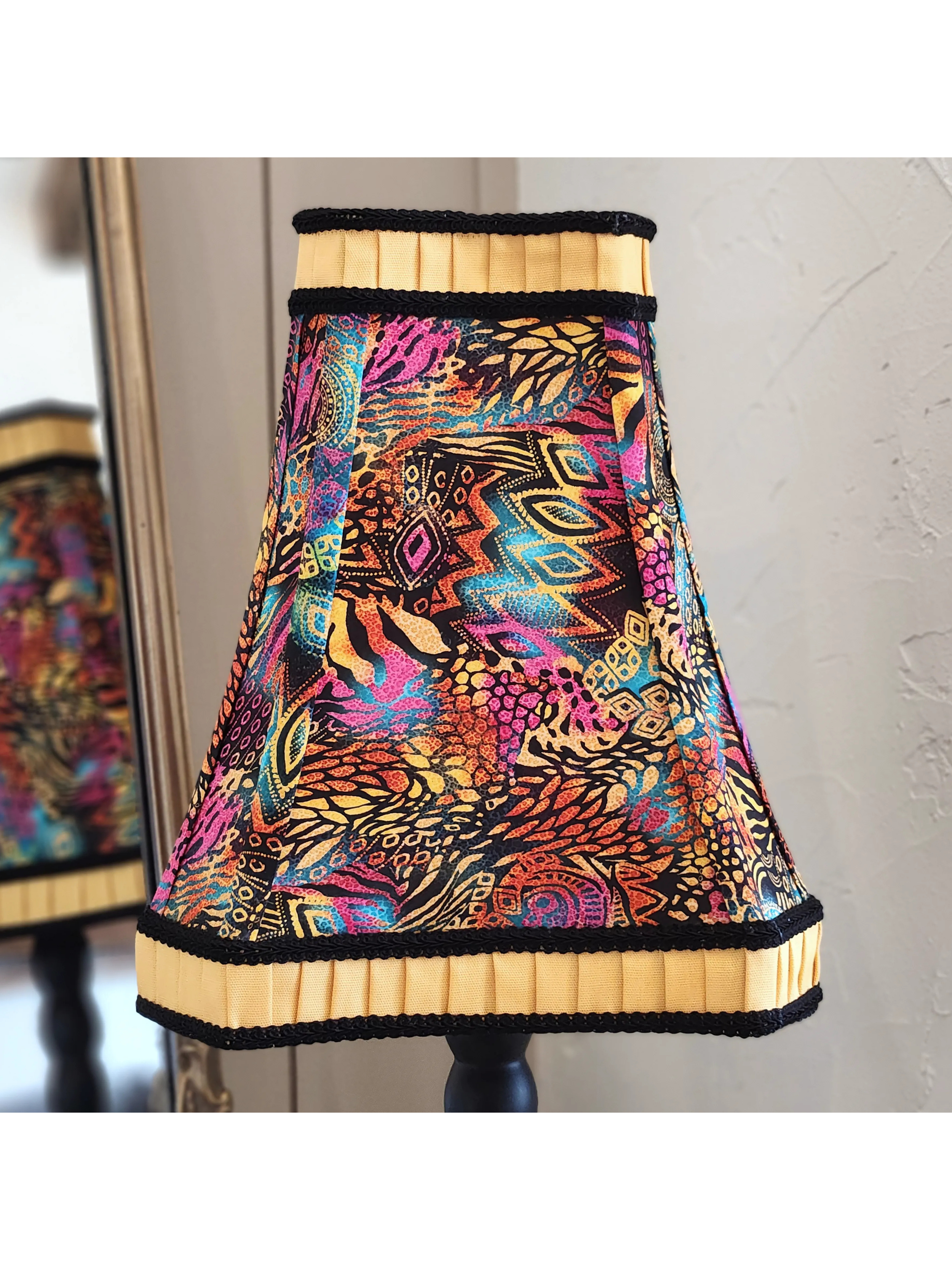 Colorful patterned lamp shade with black trim on a dark lamp base, reflected in the mirror behind.