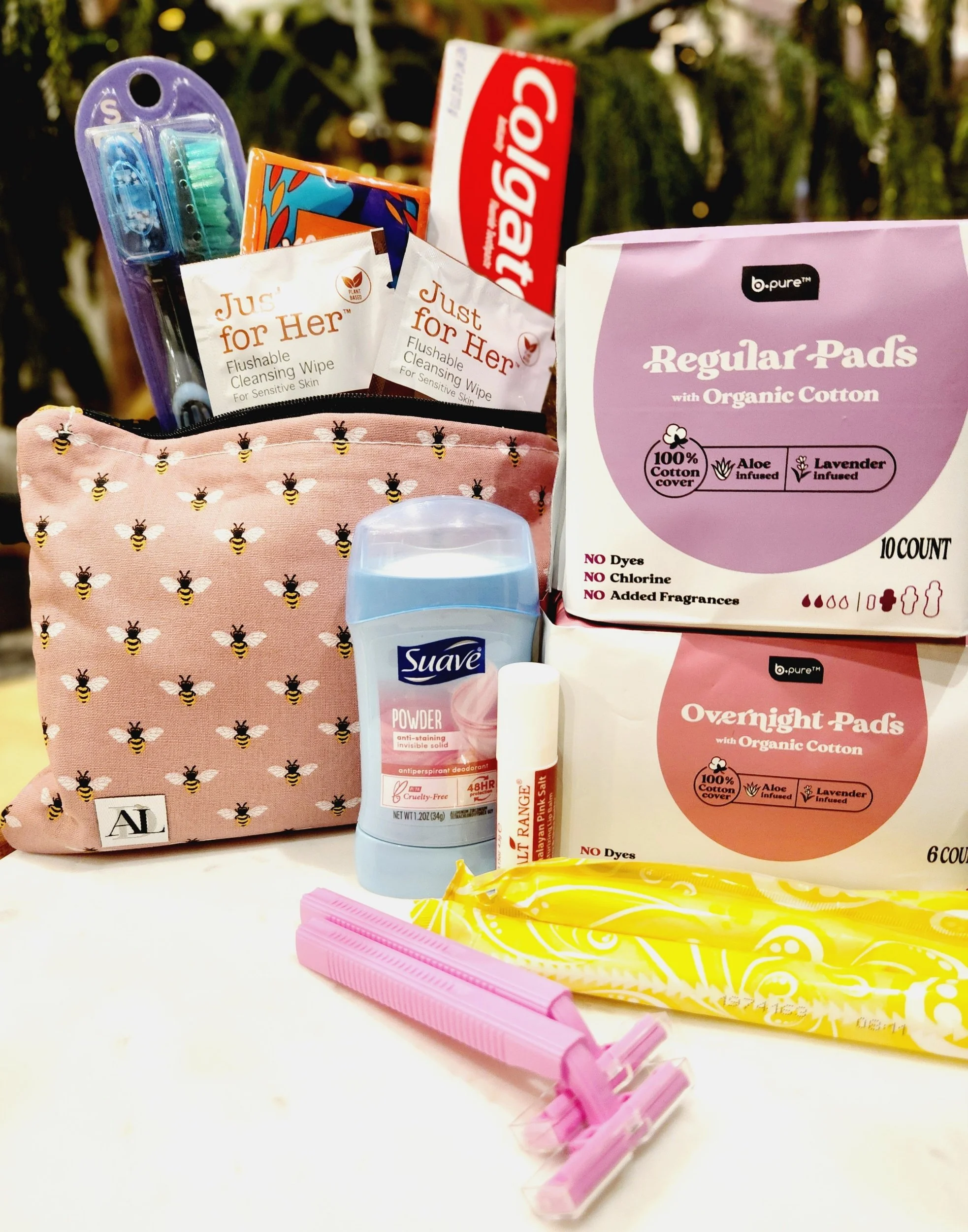 Assorted personal care products including toothpaste, toothbrushes, deodorant, sanitary pads, cleansing wipes, razors, a lip balm, and a patterned pouch.