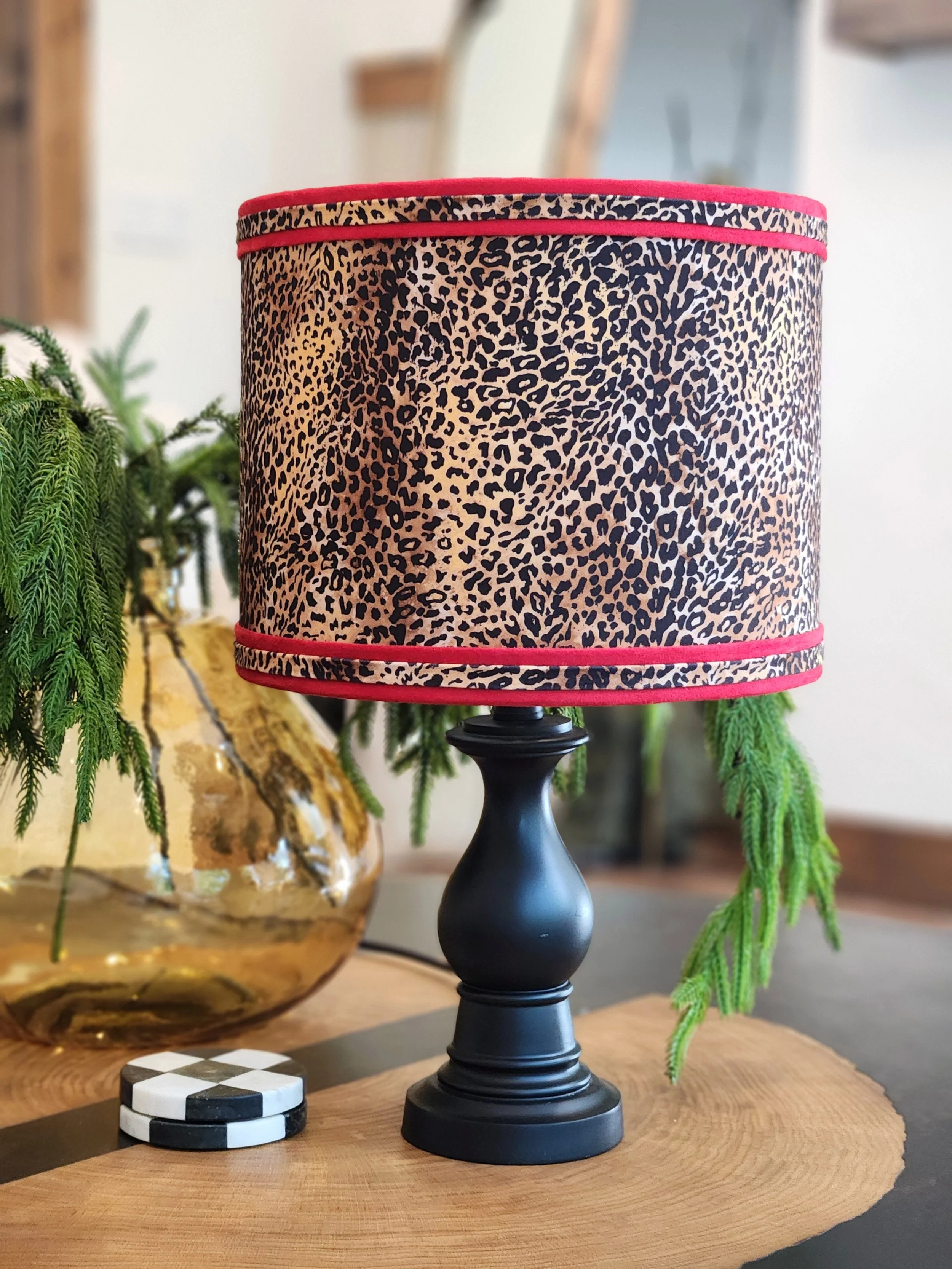 A table lamp with a black base and a cylindrical shade featuring a leopard print pattern and a red trim.
