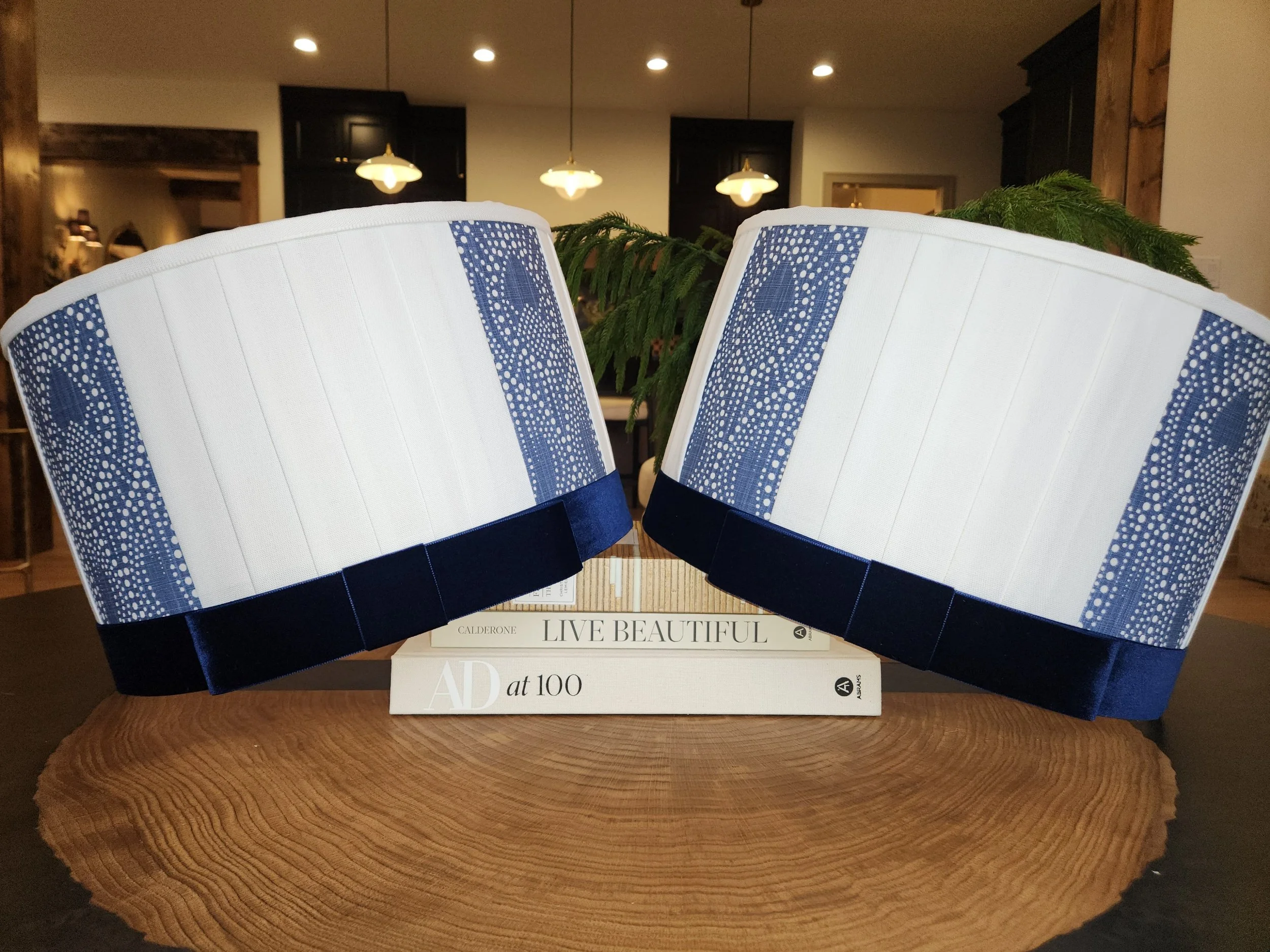 Two blue and white decorative drum lampshades with a dotted pattern, displayed on top of a stack of books on a wooden surface in a modern interior setting.
