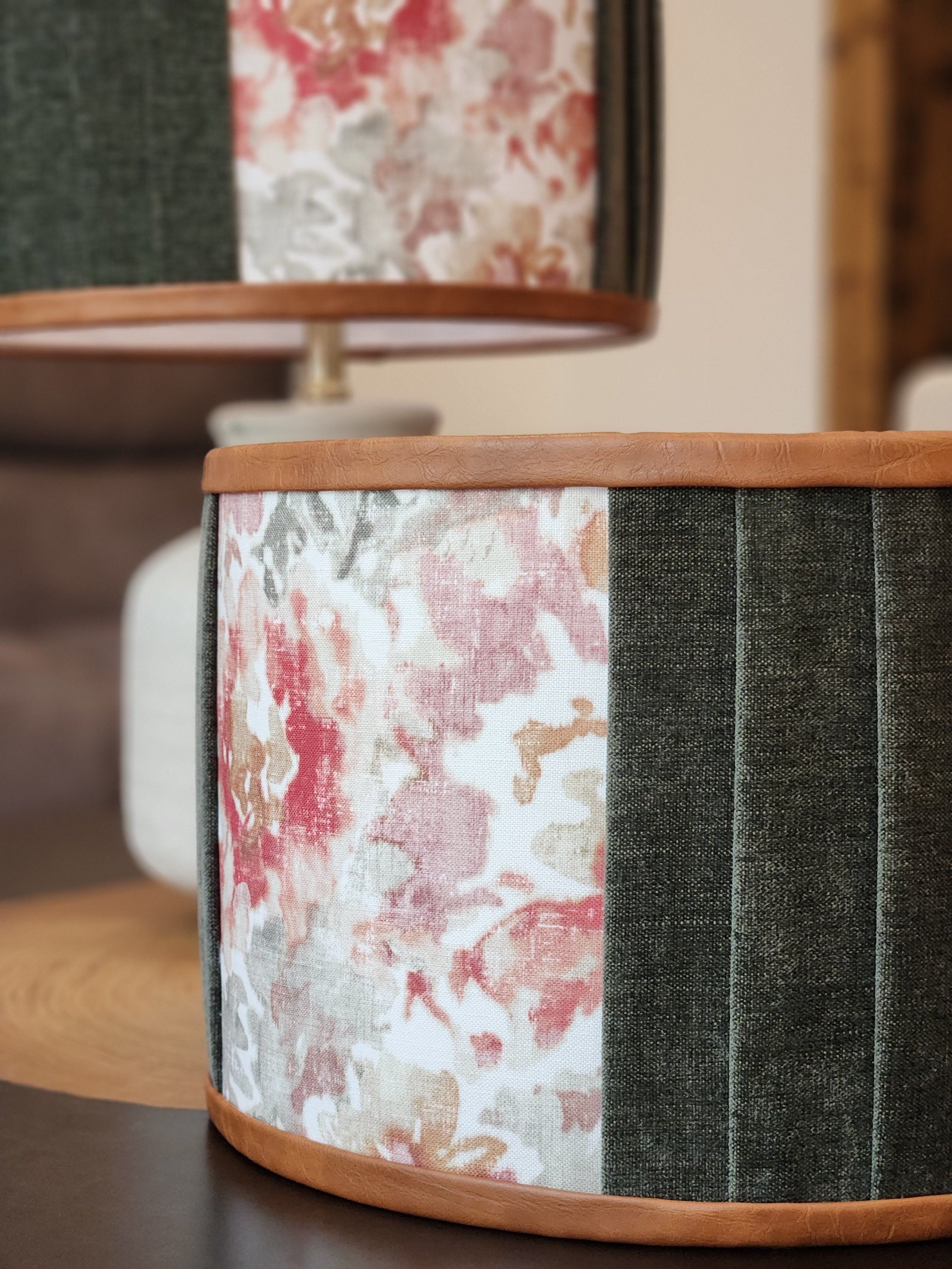 Close-up of a table lamp with a floral-patterned shade and a faux leather trim, placed on a dark surface.