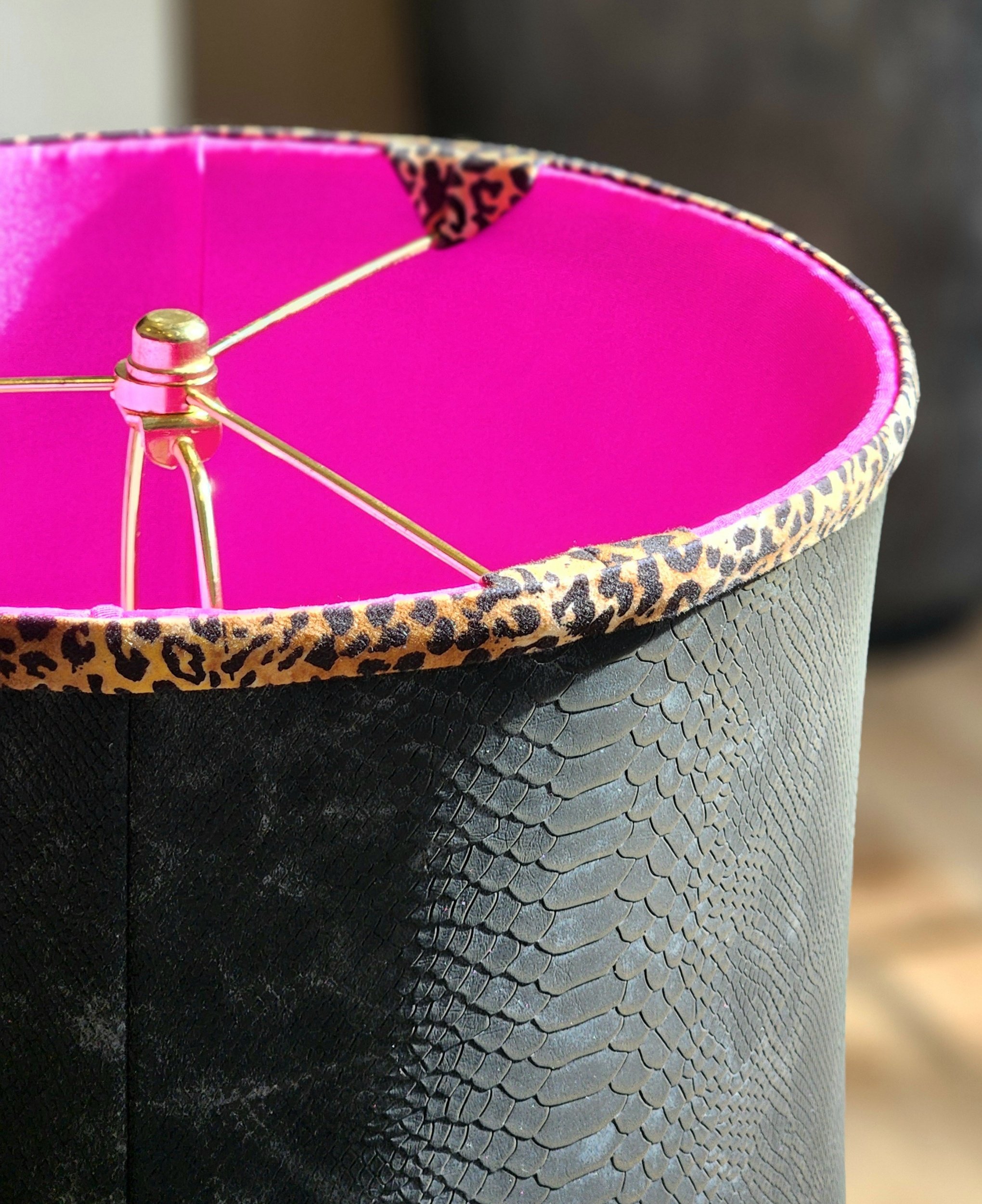 Close-up of a black textured cylindrical lampshade with leopard print trim inside and a bright pink interior, showing the metal frame and support wires.