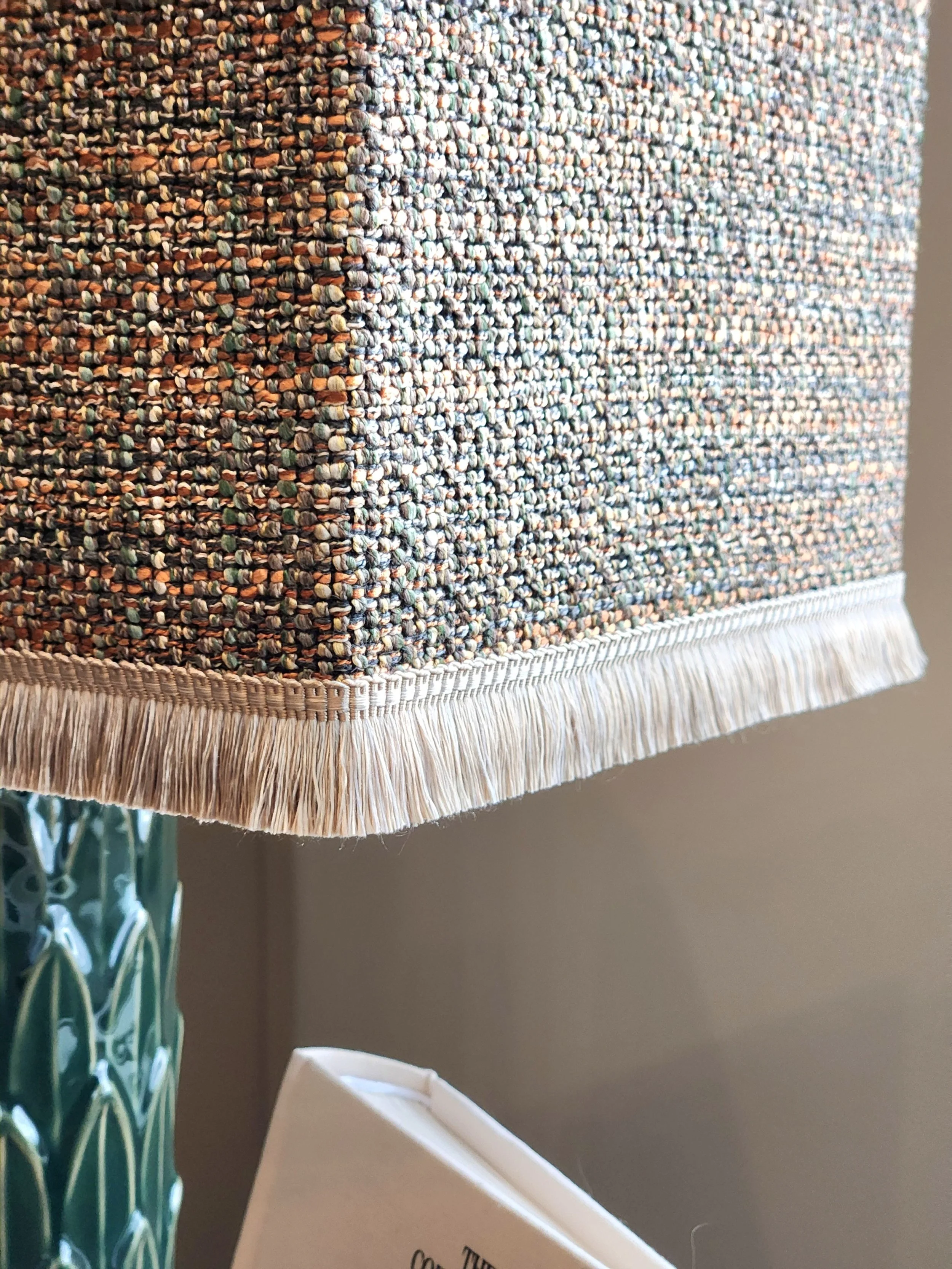 Close-up of a multicolored woven fabric lampshade with beige fringe along the bottom edge.