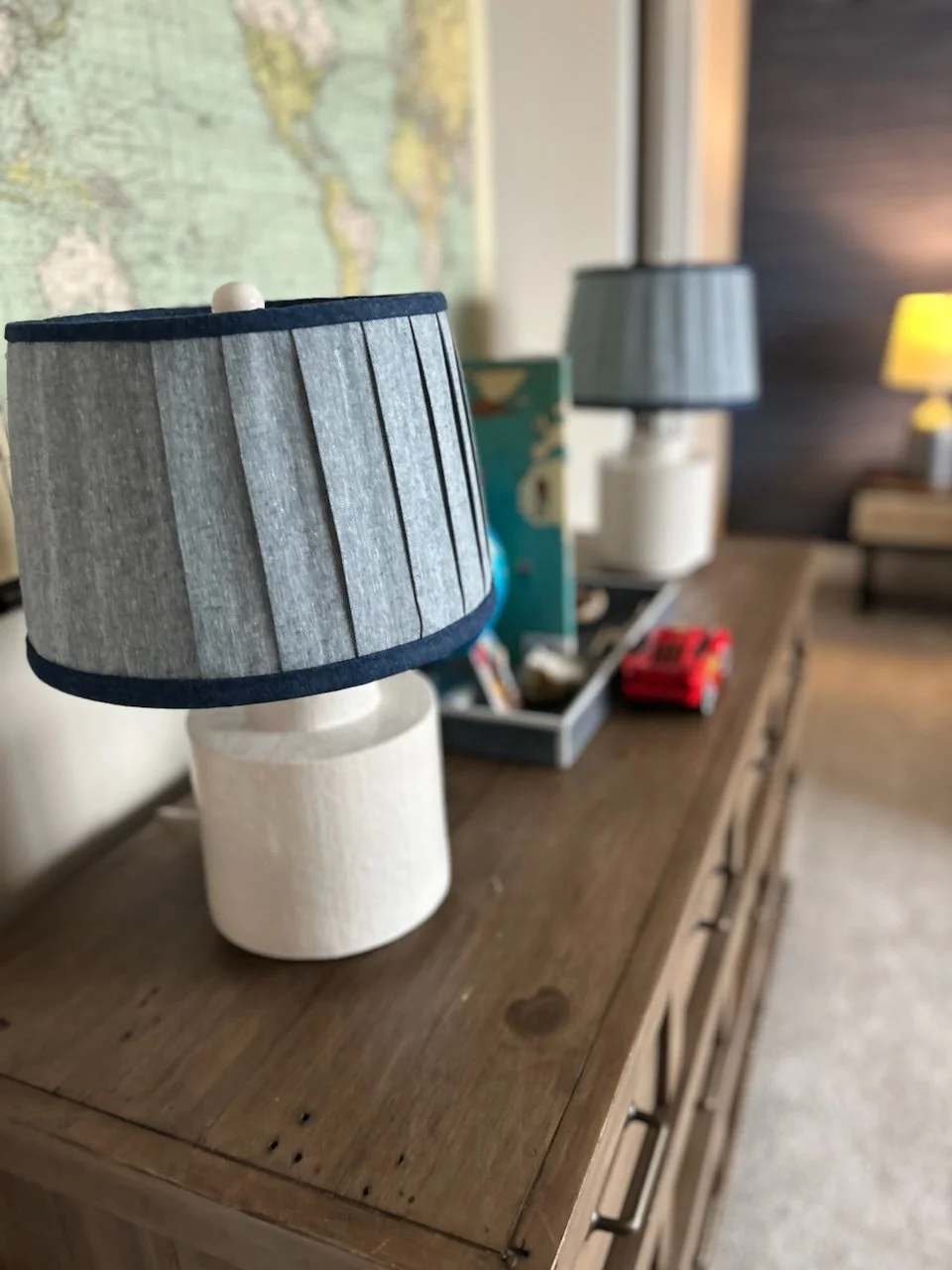 Wooden dresser with two table lamps, map on wall, small toy car.