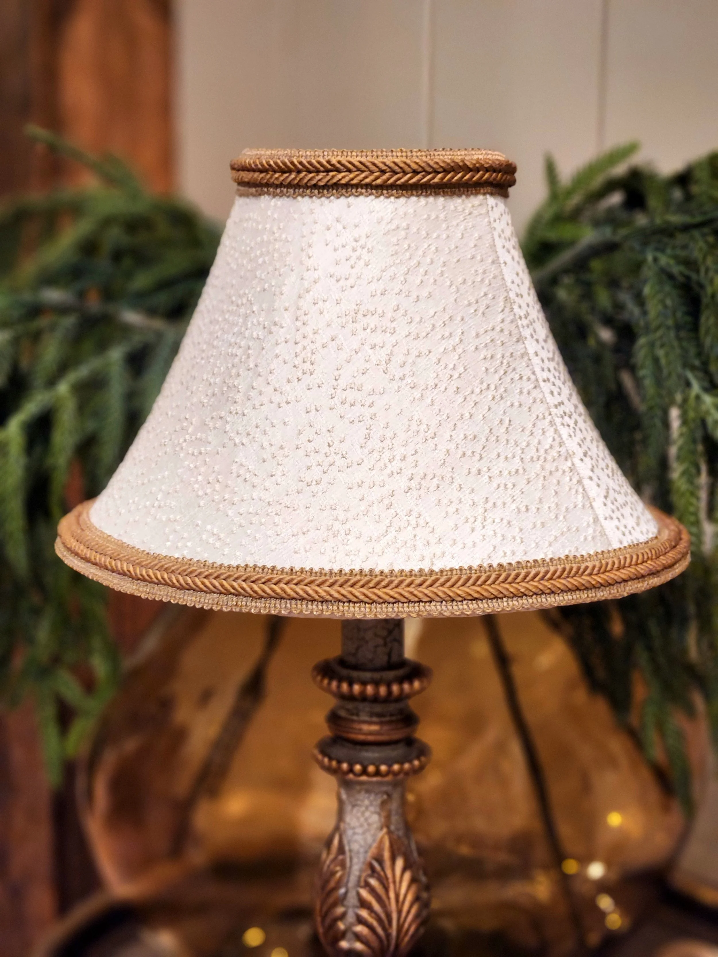 A decorative table lamp with a textured white lampshade and intricate detailing on the base, set against a cozy indoor setting.