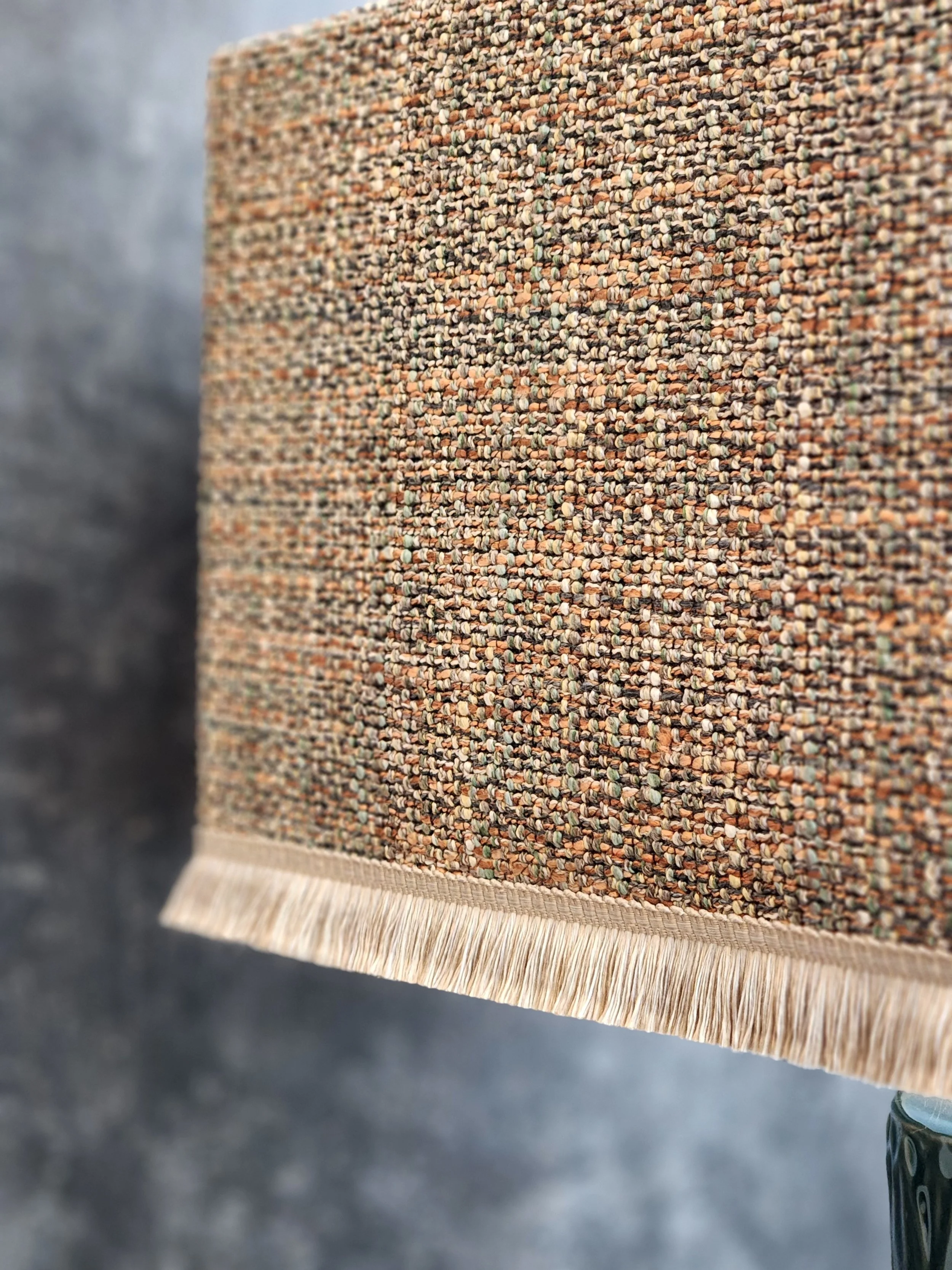 Close-up of a multi-colored textured lampshade with fringed edges, hanging vertically.